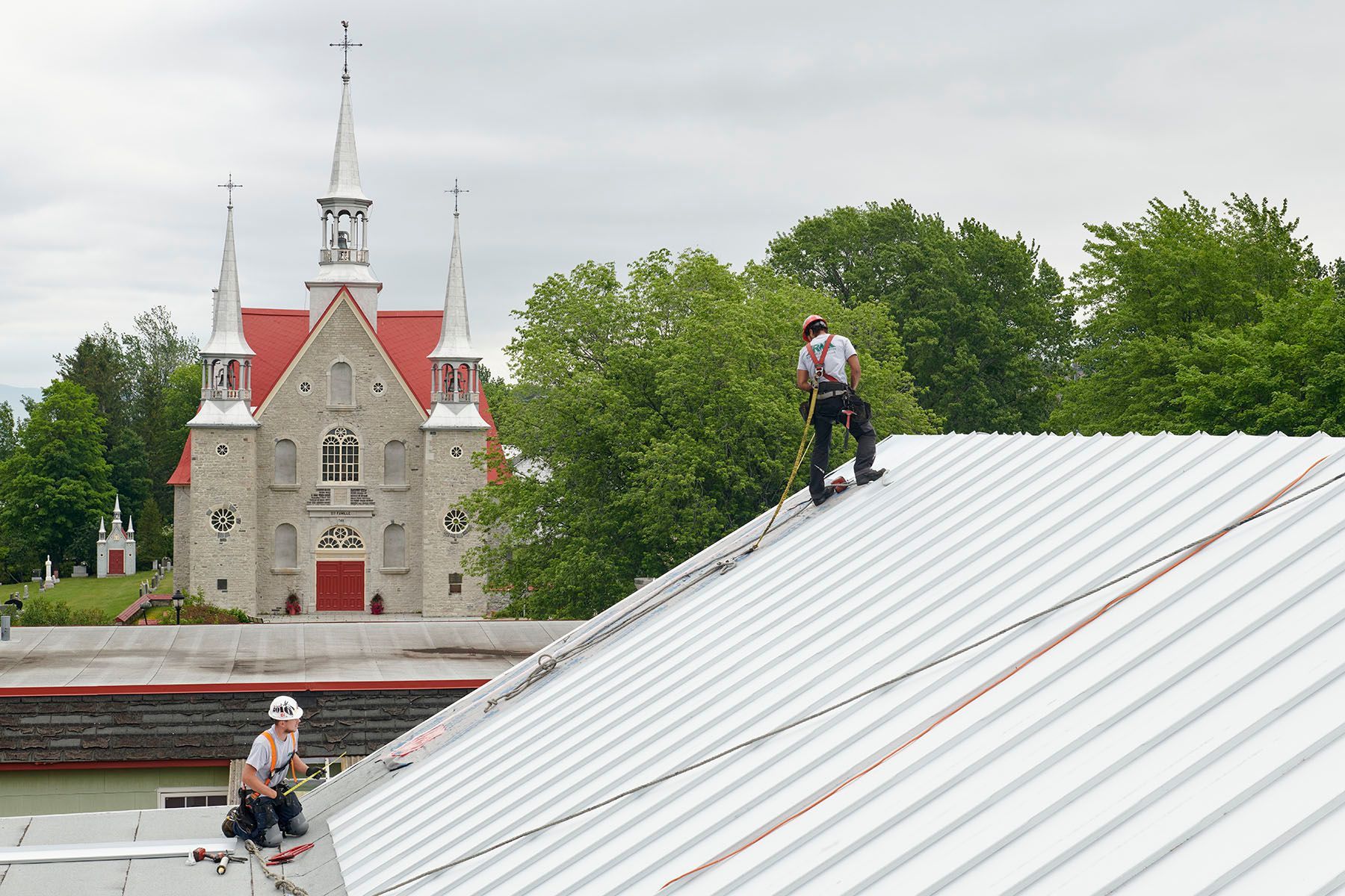 Deux hommes travaillent sur le toit d'un bâtiment avec une église en arrière-plan.