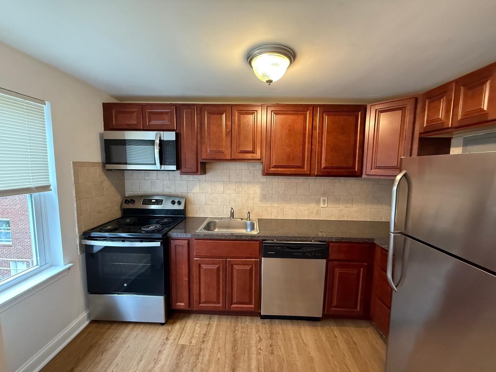 Apartment kitchen with wooden cabinetry, stainless steel appliances, and window