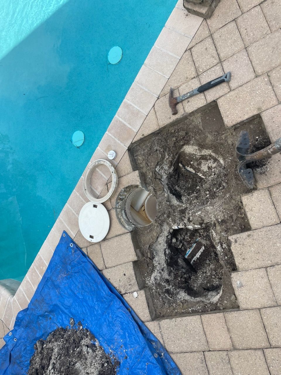 Pool equipment being excavated from brick patio near pool. Tools and debris visible.
