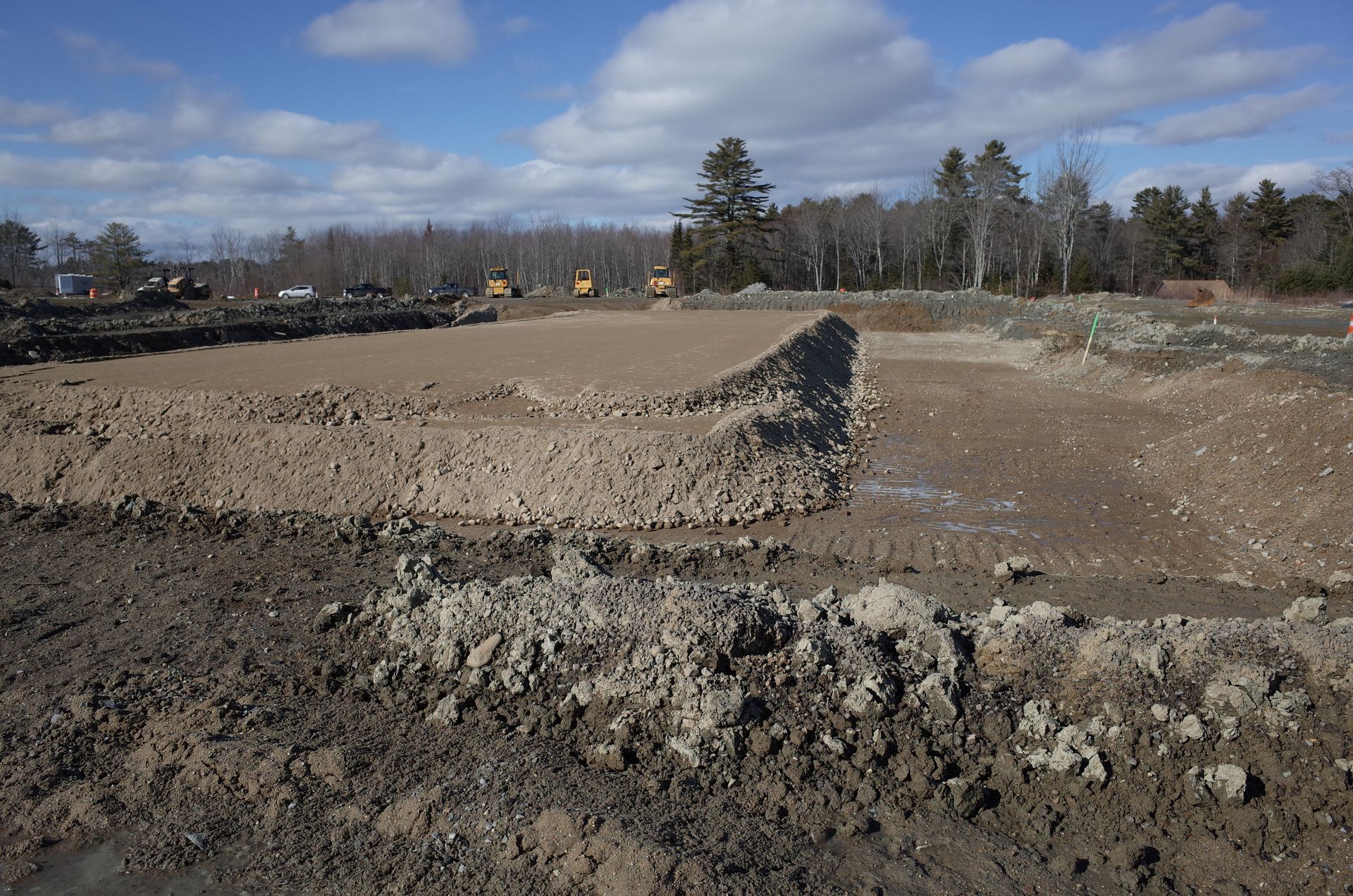 Dirt construction site with a large mound and muddy ground under a clear sky