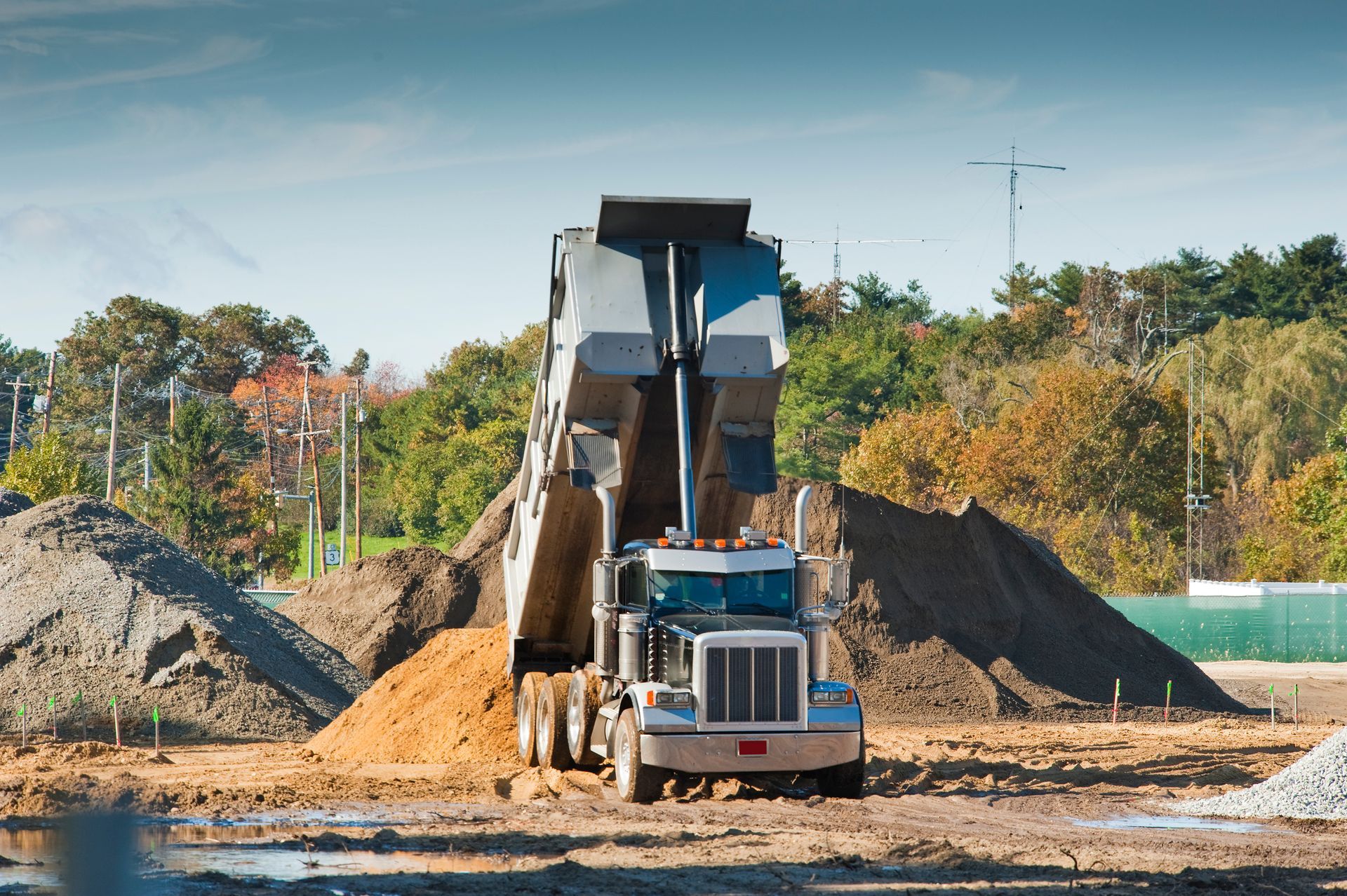 Dump truck unloading a large pile of soil in a field under a blue sky
