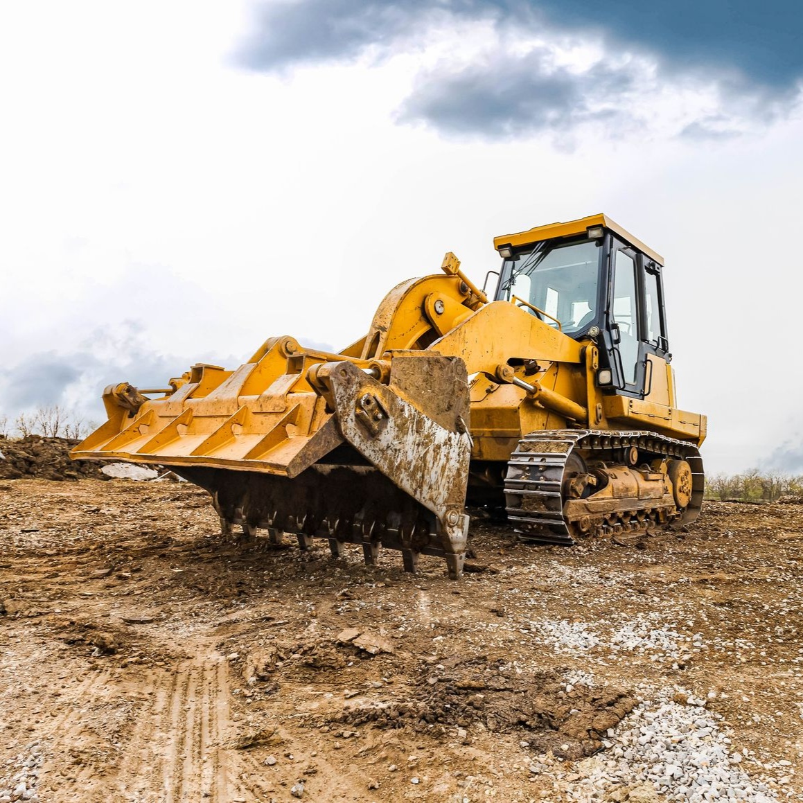 Yellow bulldozer pushing dirt on a muddy construction site under a cloudy sky