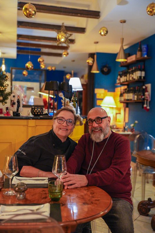 Due persone sorridenti sedute a un tavolo in un ristorante con decorazioni dorate e pareti blu.