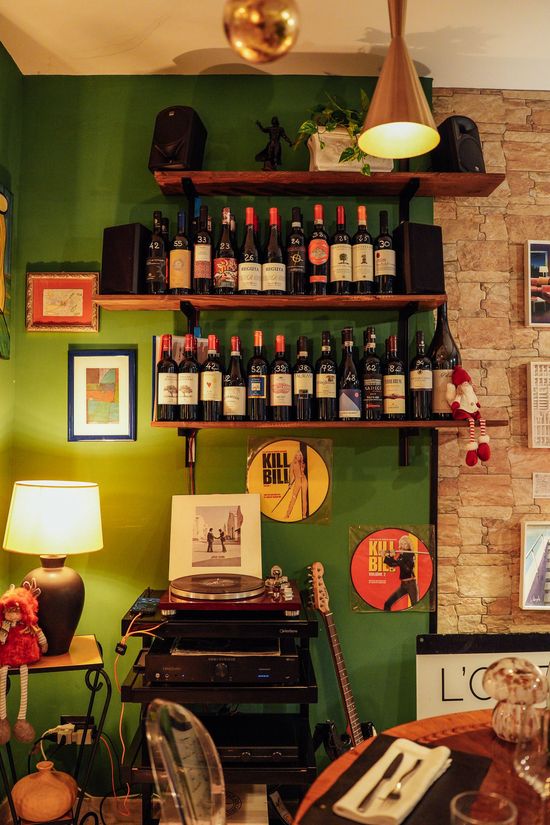 Interno di un ristorante con pareti verdi, dettagli in mattoni, scaffali pieni di vino e apparecchiature audio.