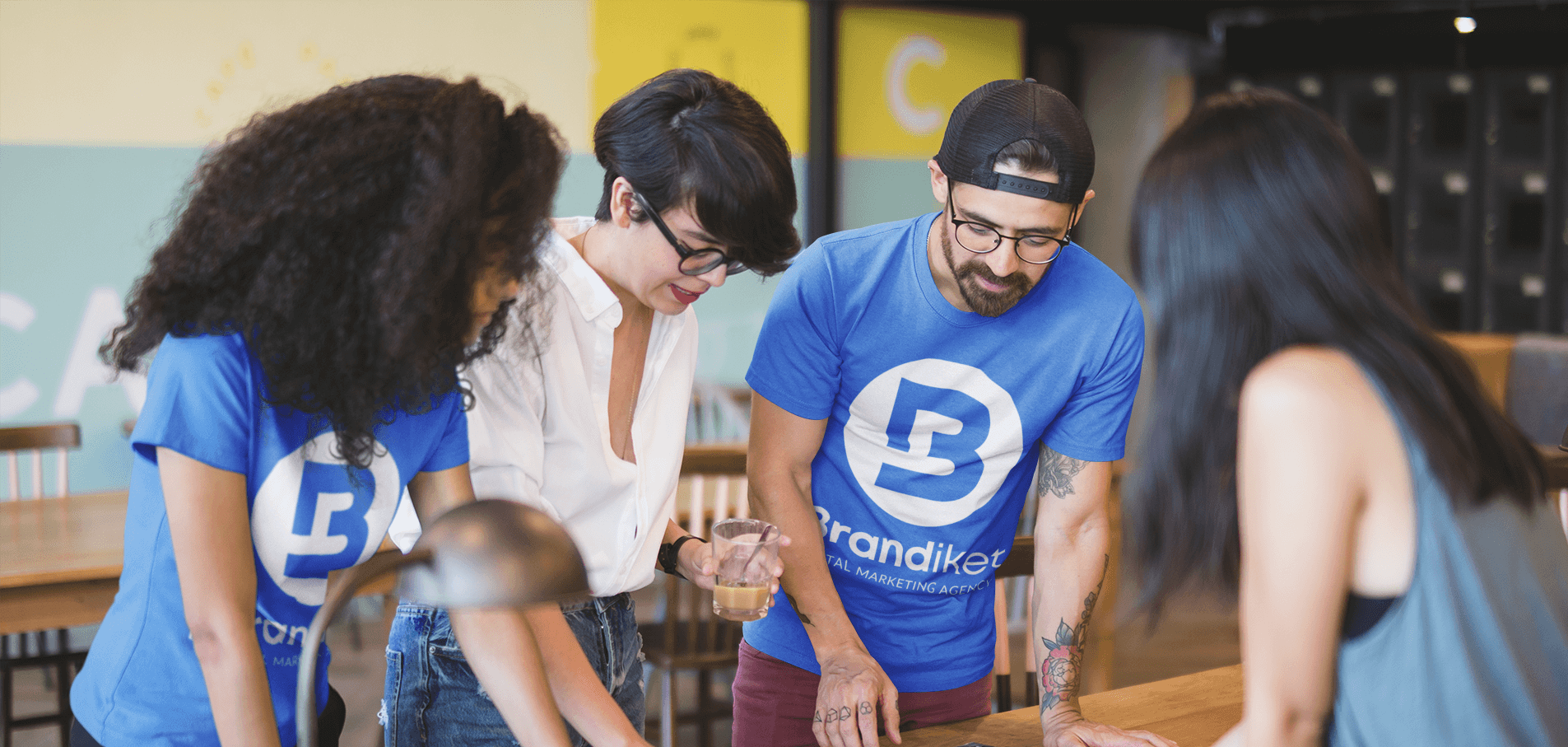 People in blue and white shirts leaning over a table in a classroom or workshop setting