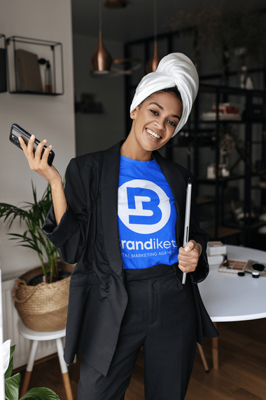 Smiling person in black blazer and blue shirt posing indoors with towel wrapped on head