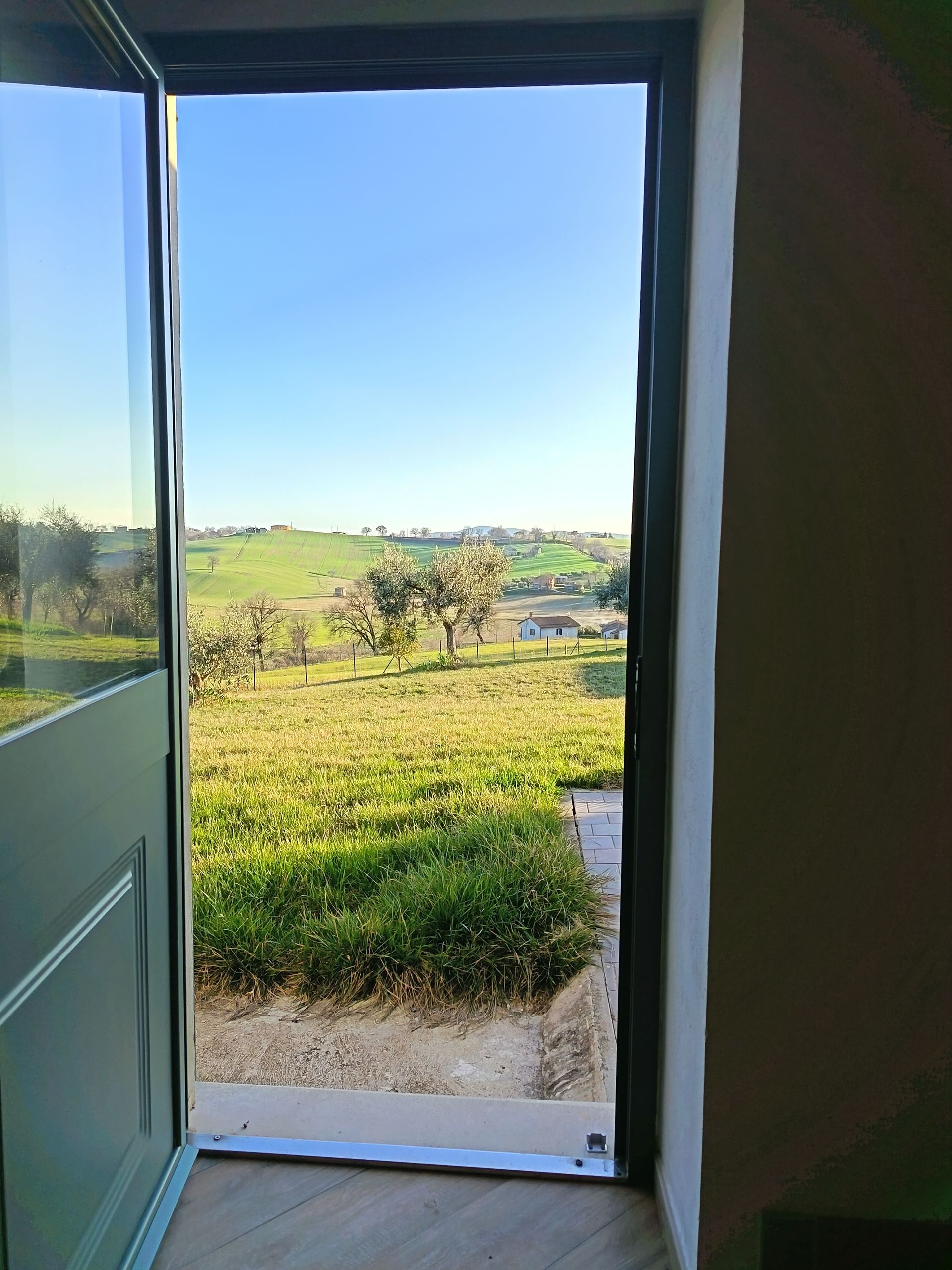Una porta verde aperta incornicia la vista di un paesaggio soleggiato con dolci 