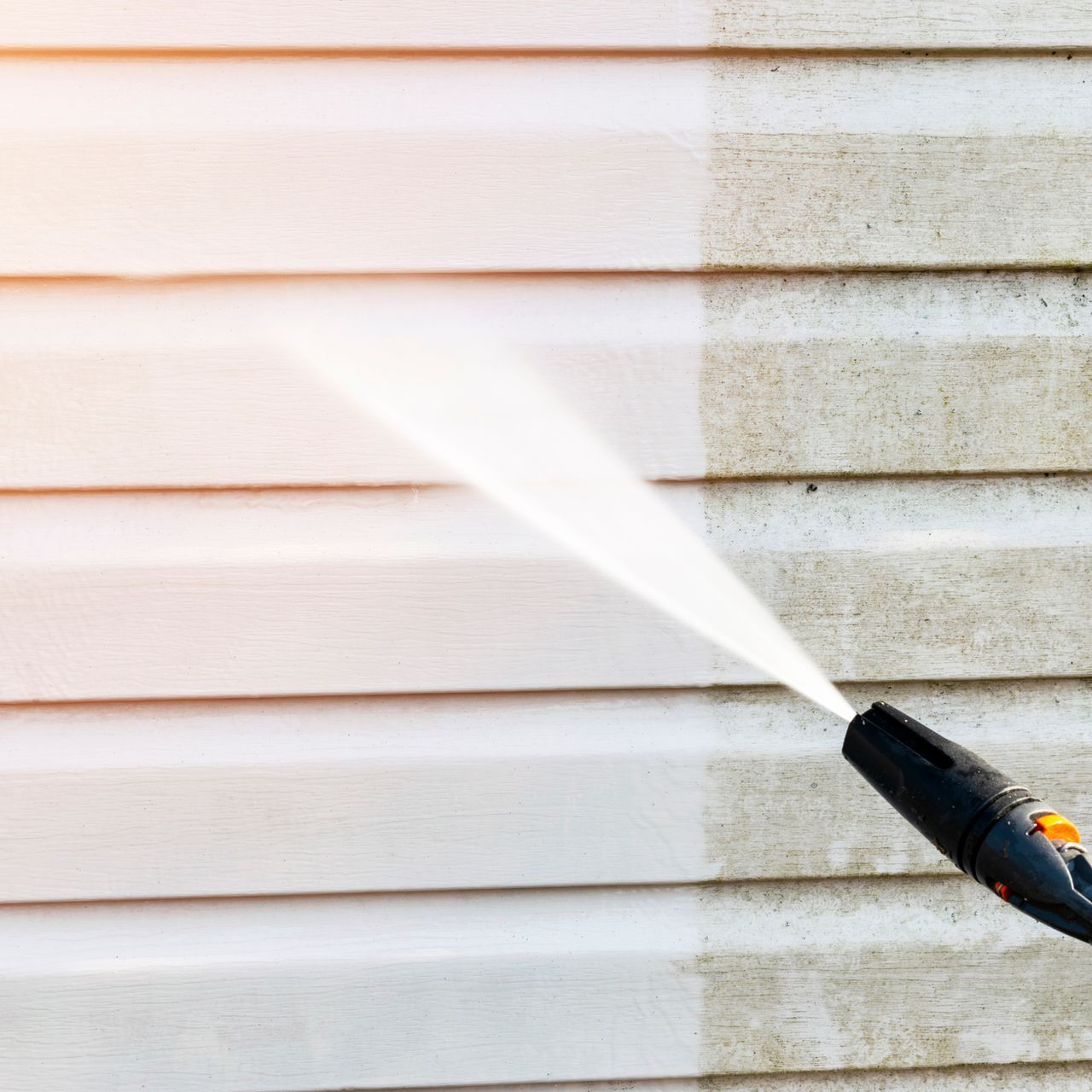 A person is cleaning the side of a house with a high pressure washer.