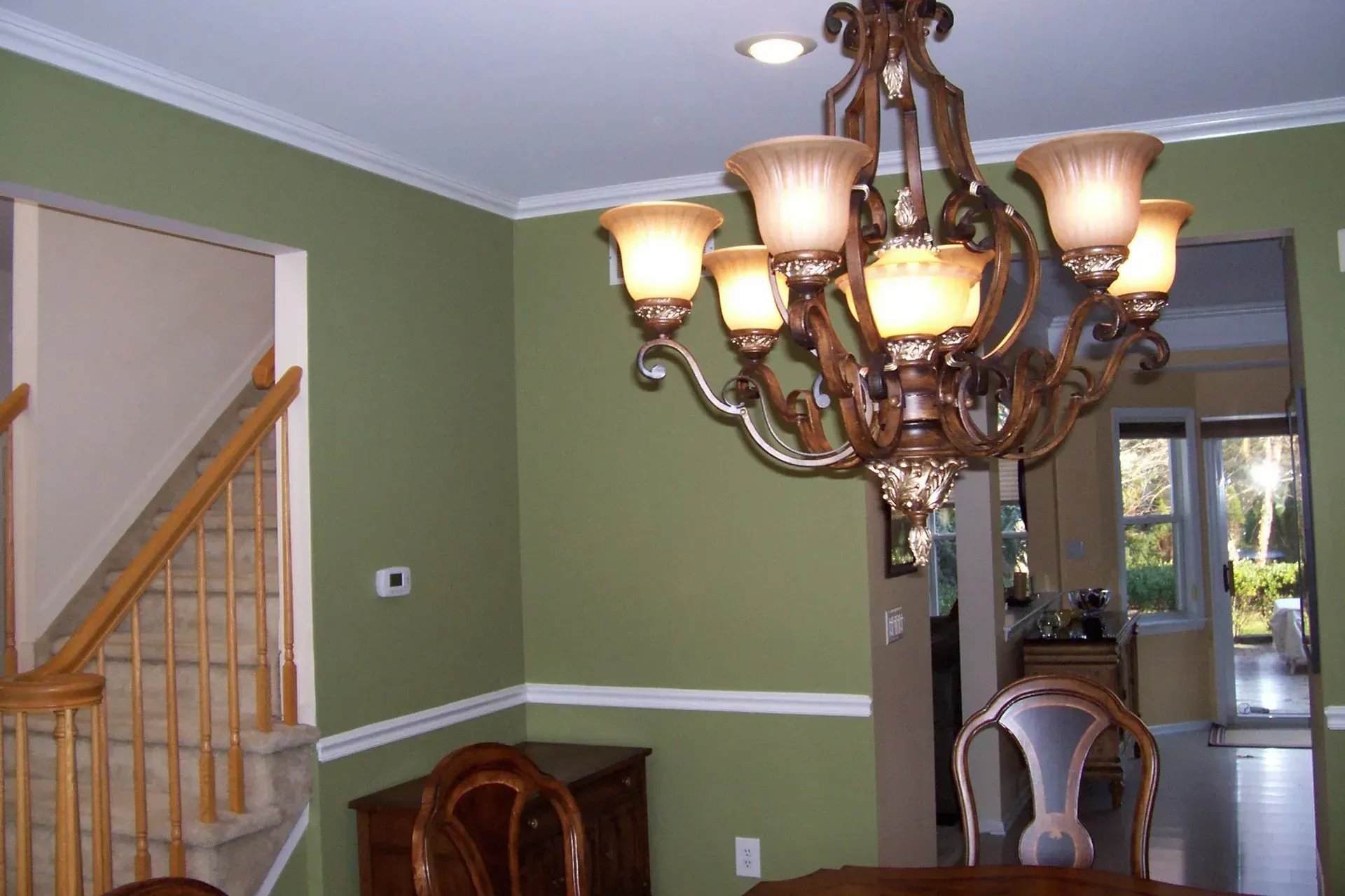 A dining room with green walls and a chandelier hanging from the ceiling