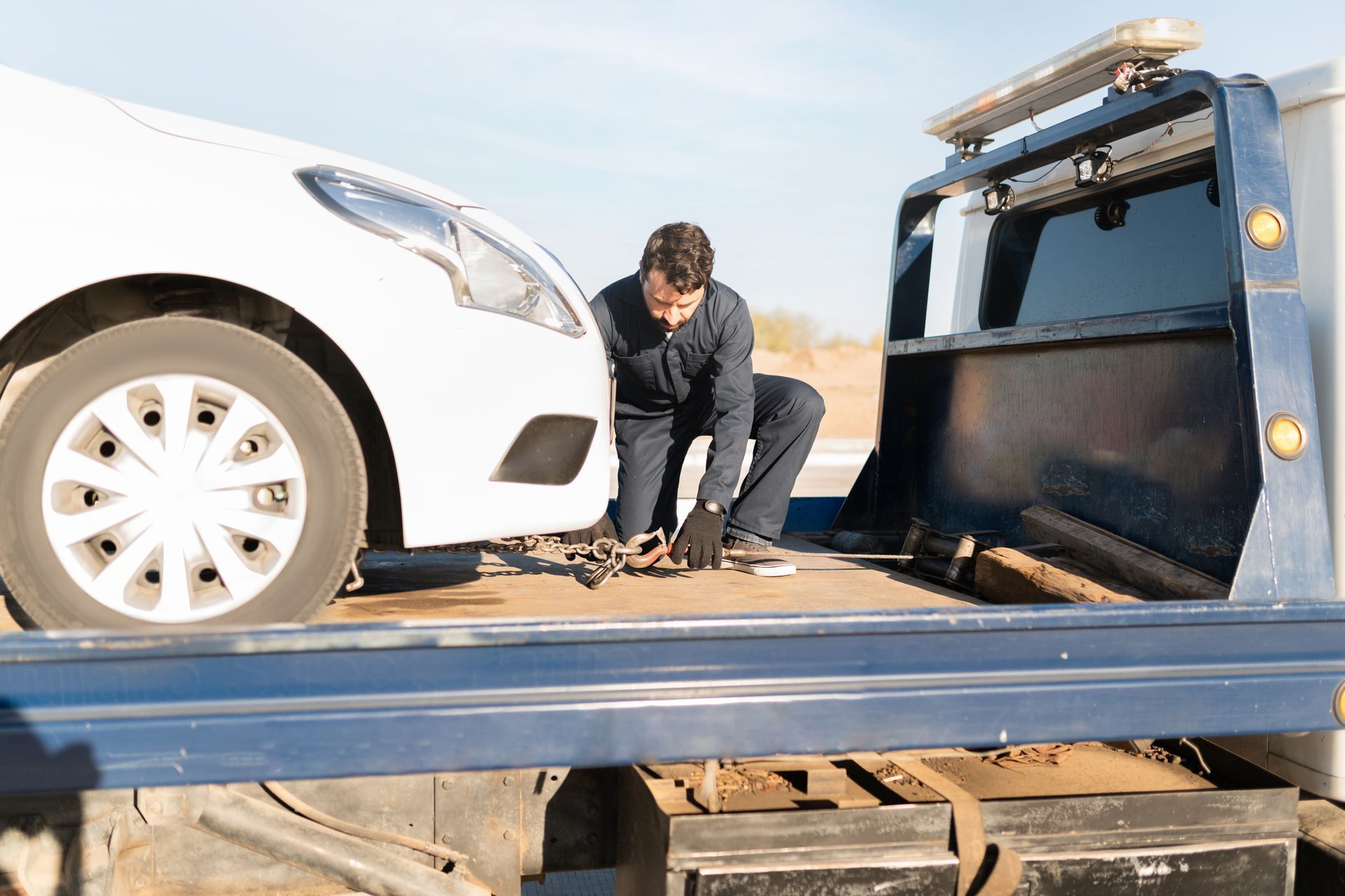 A male worker towing a broken-down car on a tow truck.