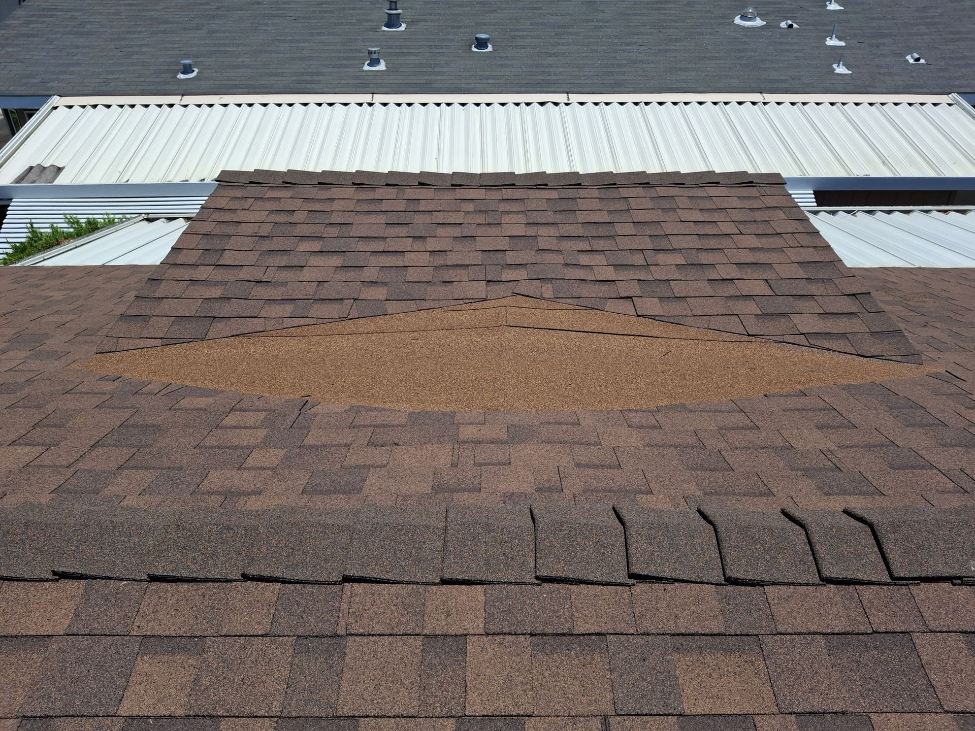 Roof with damaged shingles and a large patch of exposed underlayment near the center.