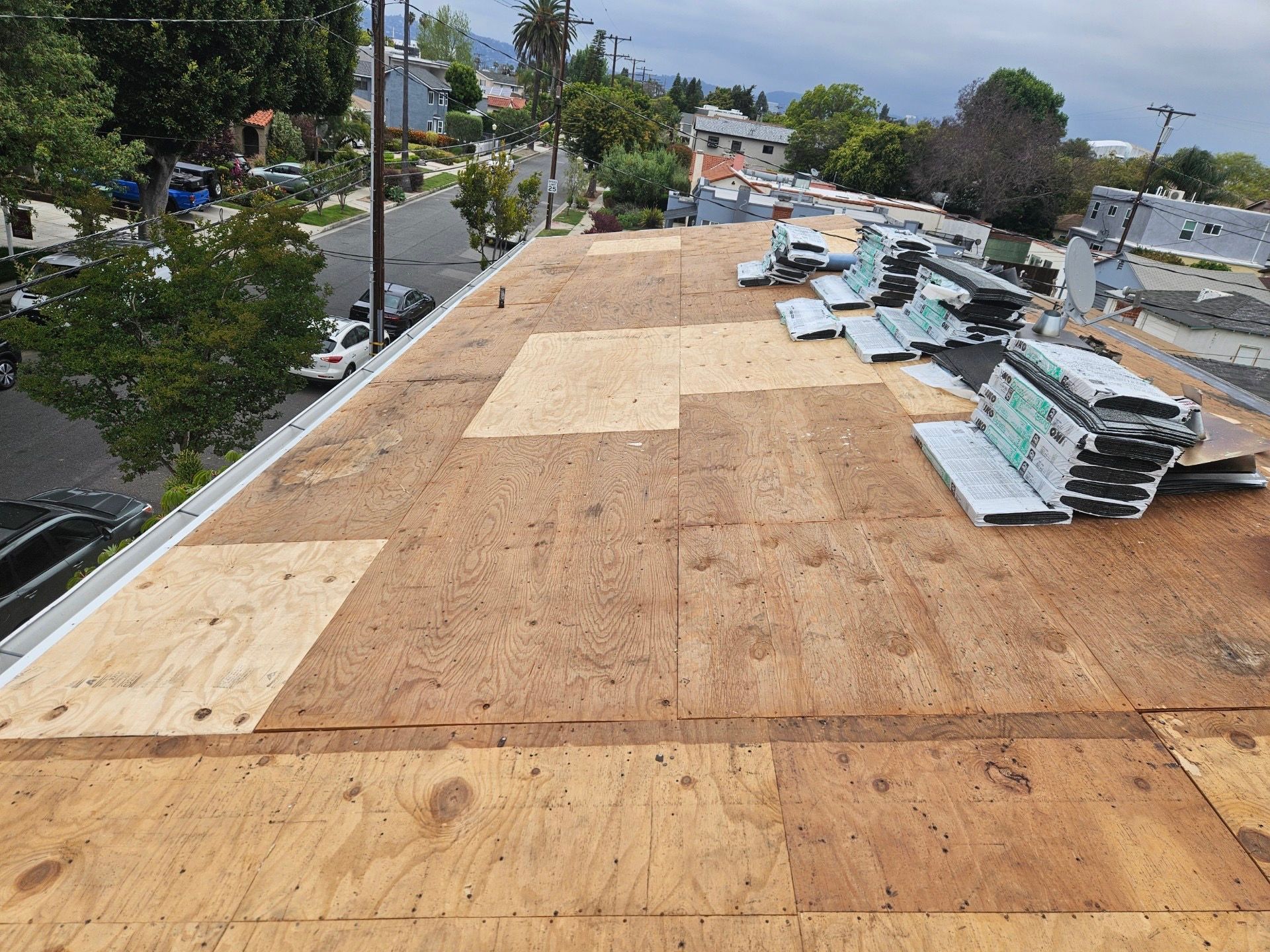 Roof under construction with plywood sheathing and stacks of materials on a residential house roof