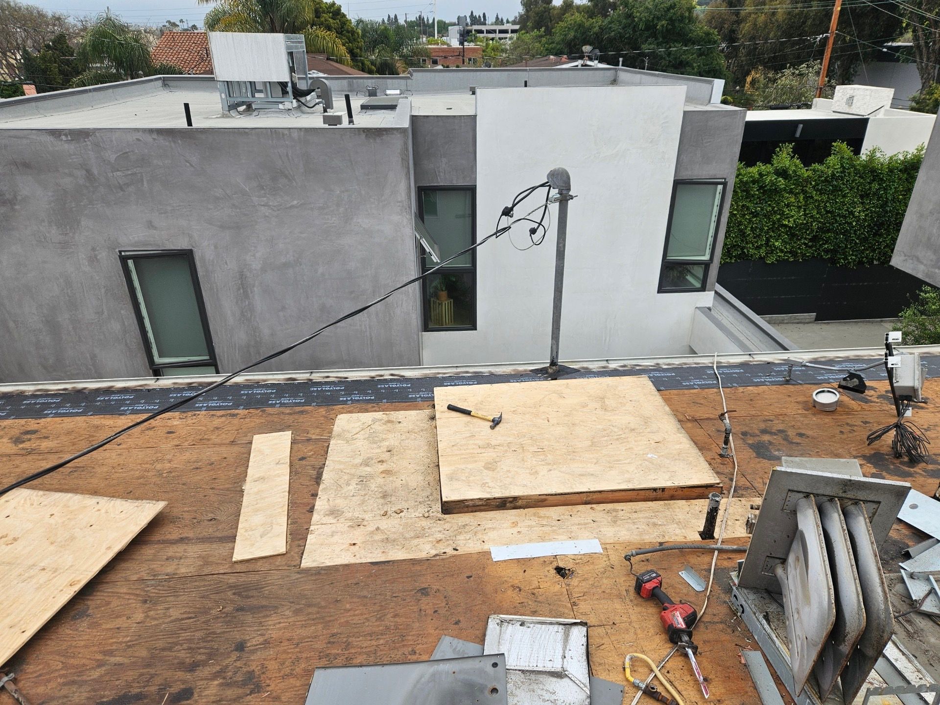 Rooftop construction area with plywood sheets, tools, and a gray building in the background.