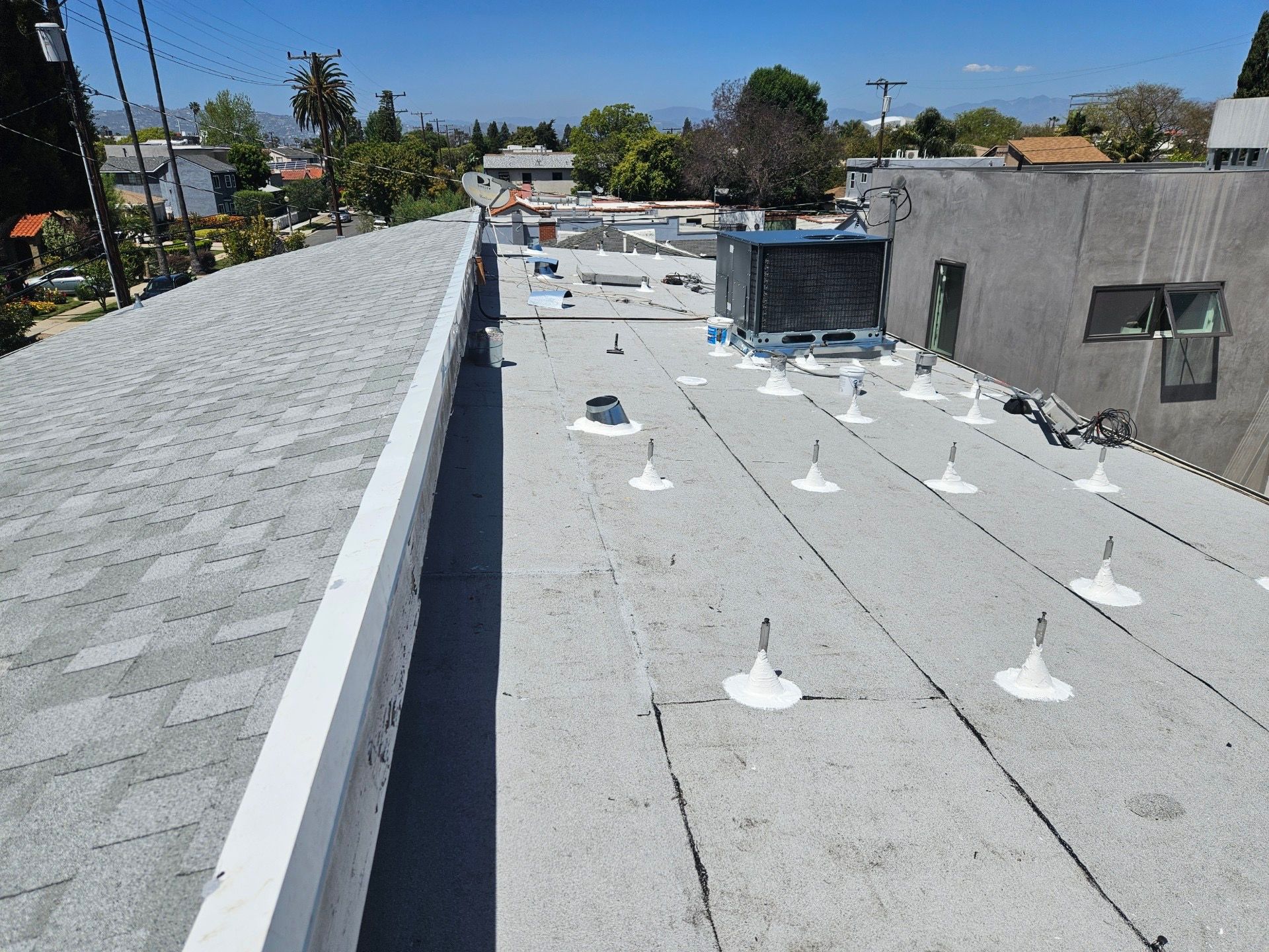 Rooftop with white protective coating, vents, and equipment under a clear blue sky