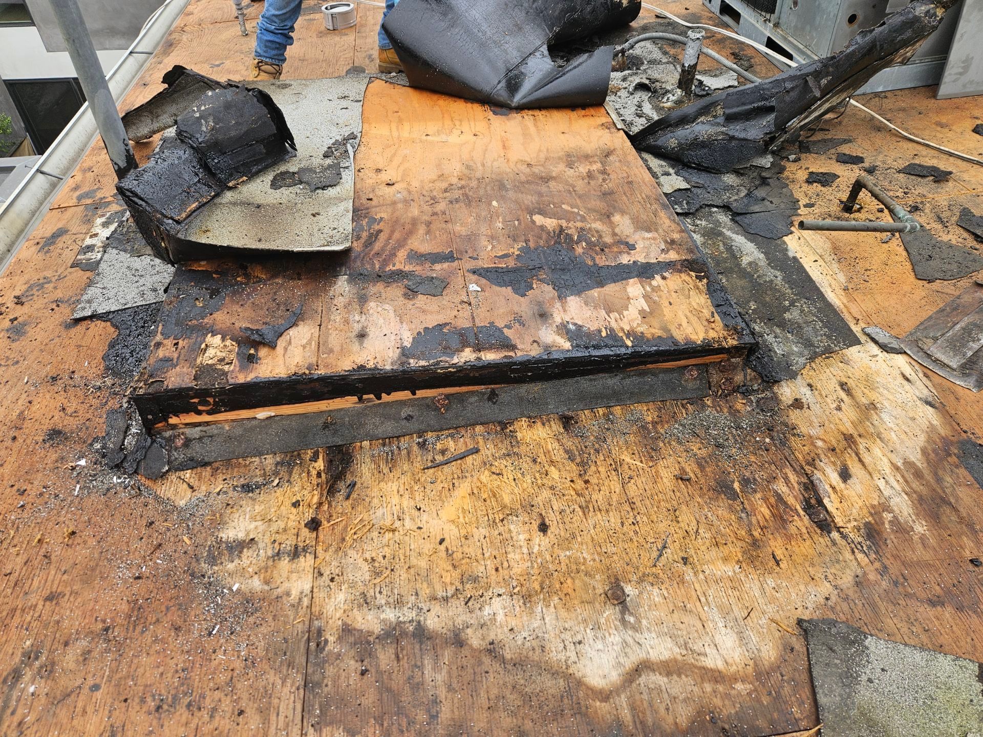 Damaged rooftop with burned, charred roofing material and debris around a rectangular repair area