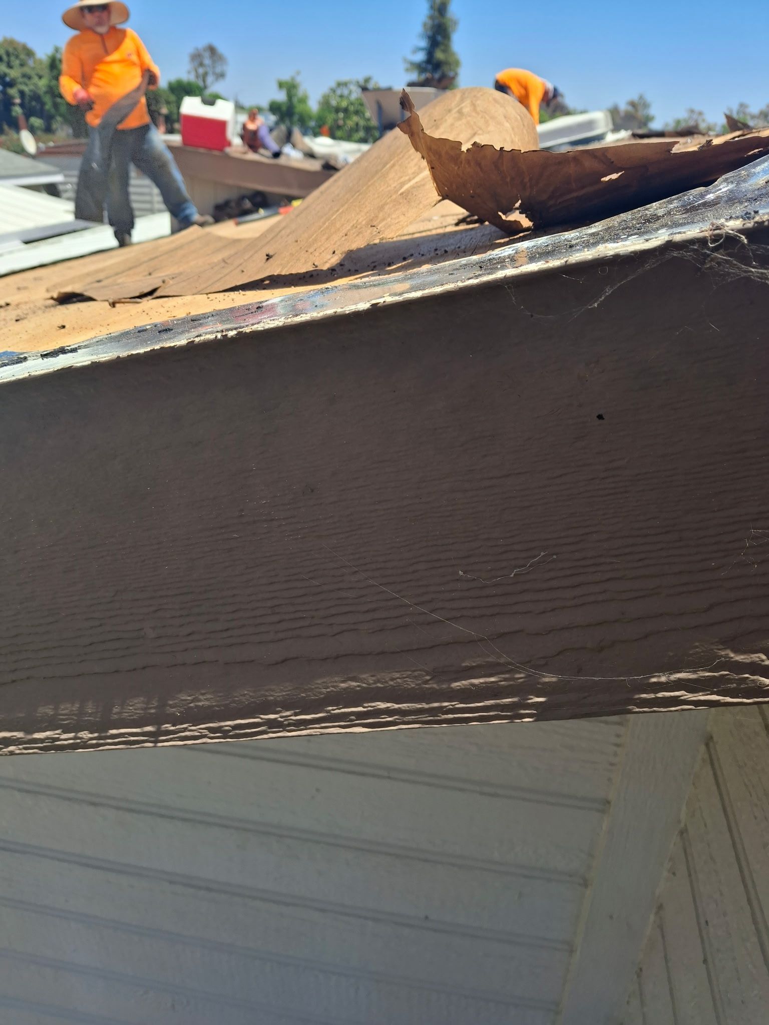 Workers in orange safety gear repairing a damaged roof with exposed plywood and torn shingles