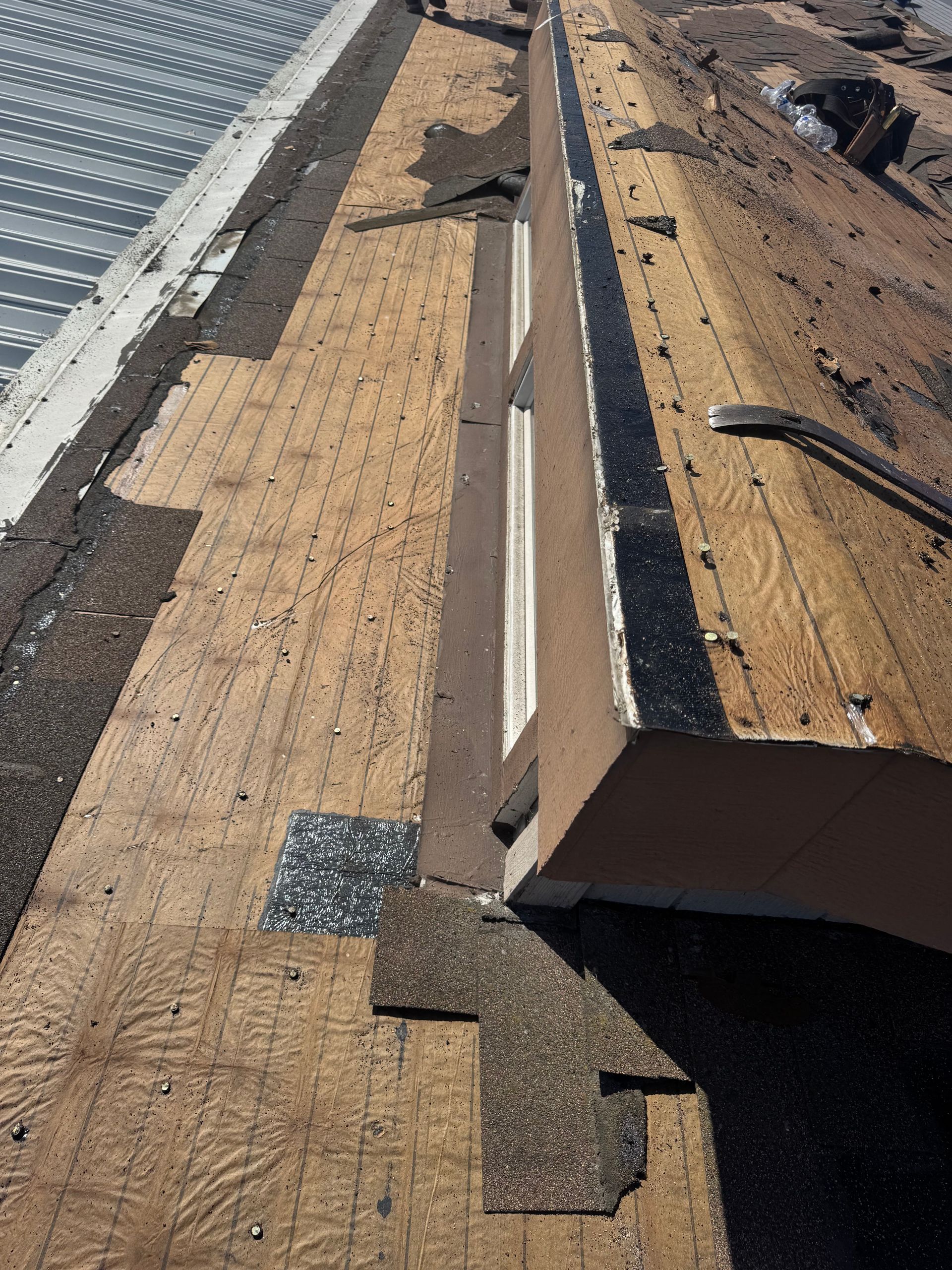 Rooftop with torn roofing felt, exposed wood, and a metal roof edge.