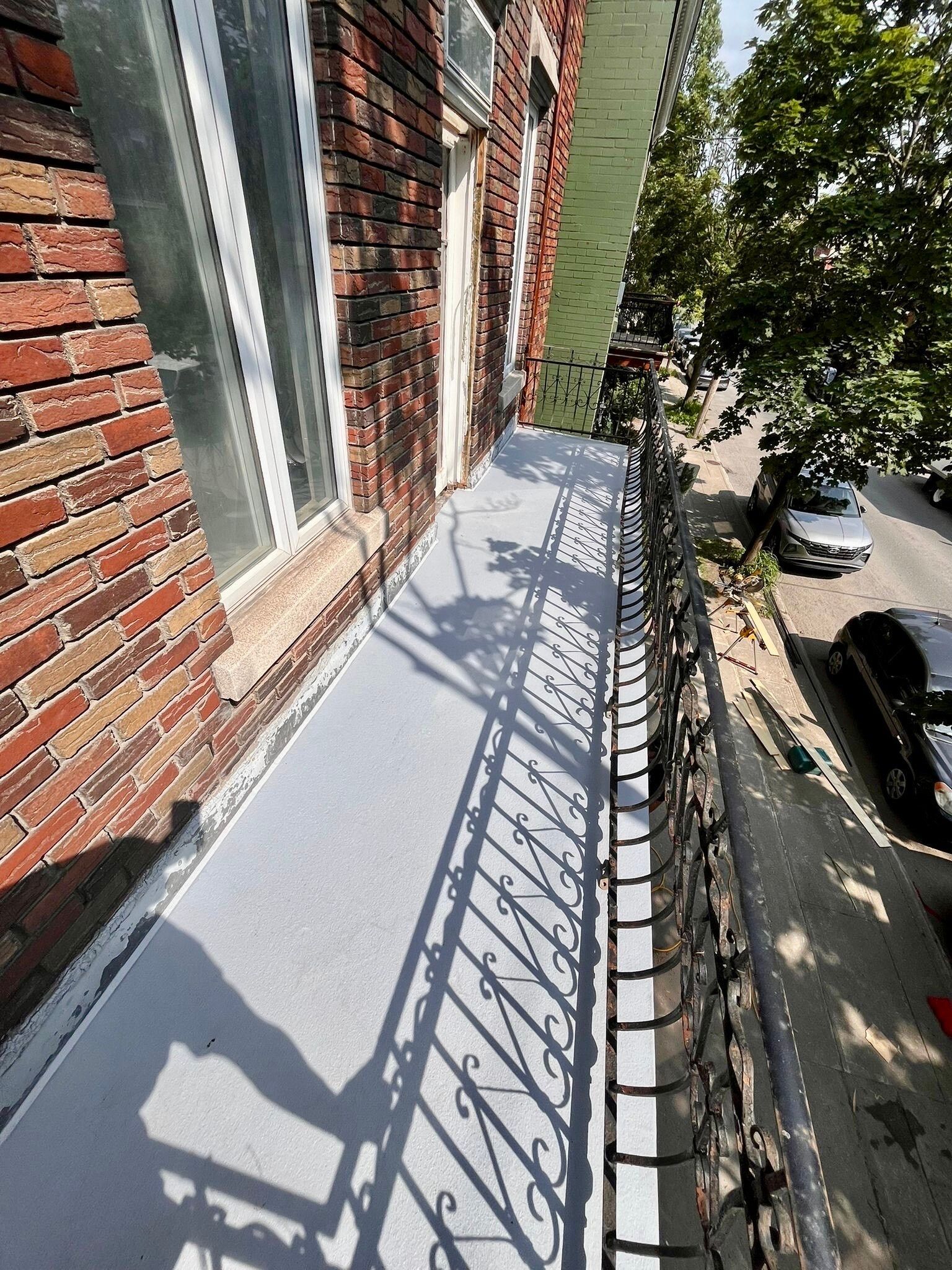 Un soudeur travaille sur un escalier en colimaçon noir fixé à un bâtiment en briques. Ciel bleu vif au-dessus.