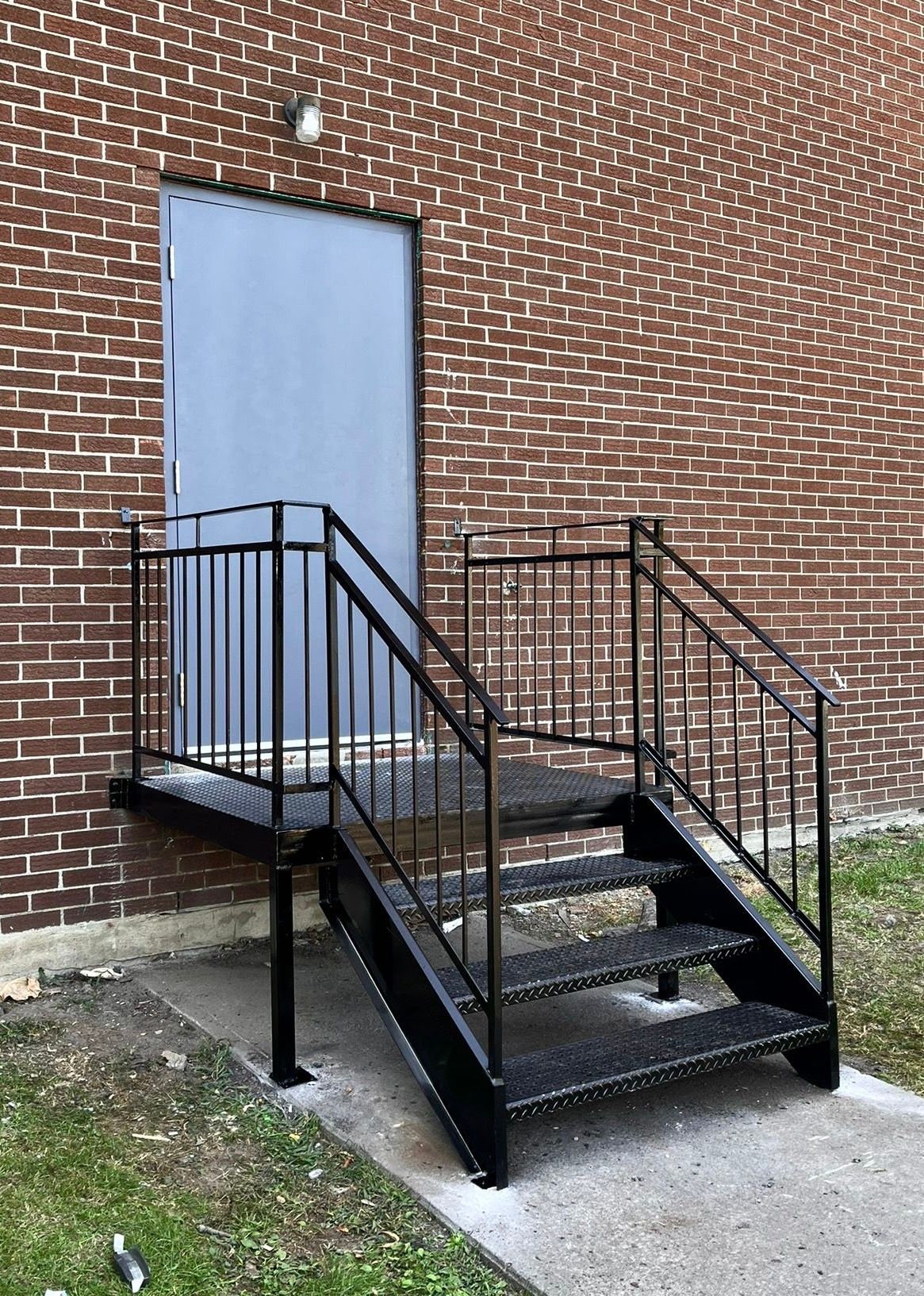 Escalier extérieur en métal menant à une porte grise sur un bâtiment en briques.