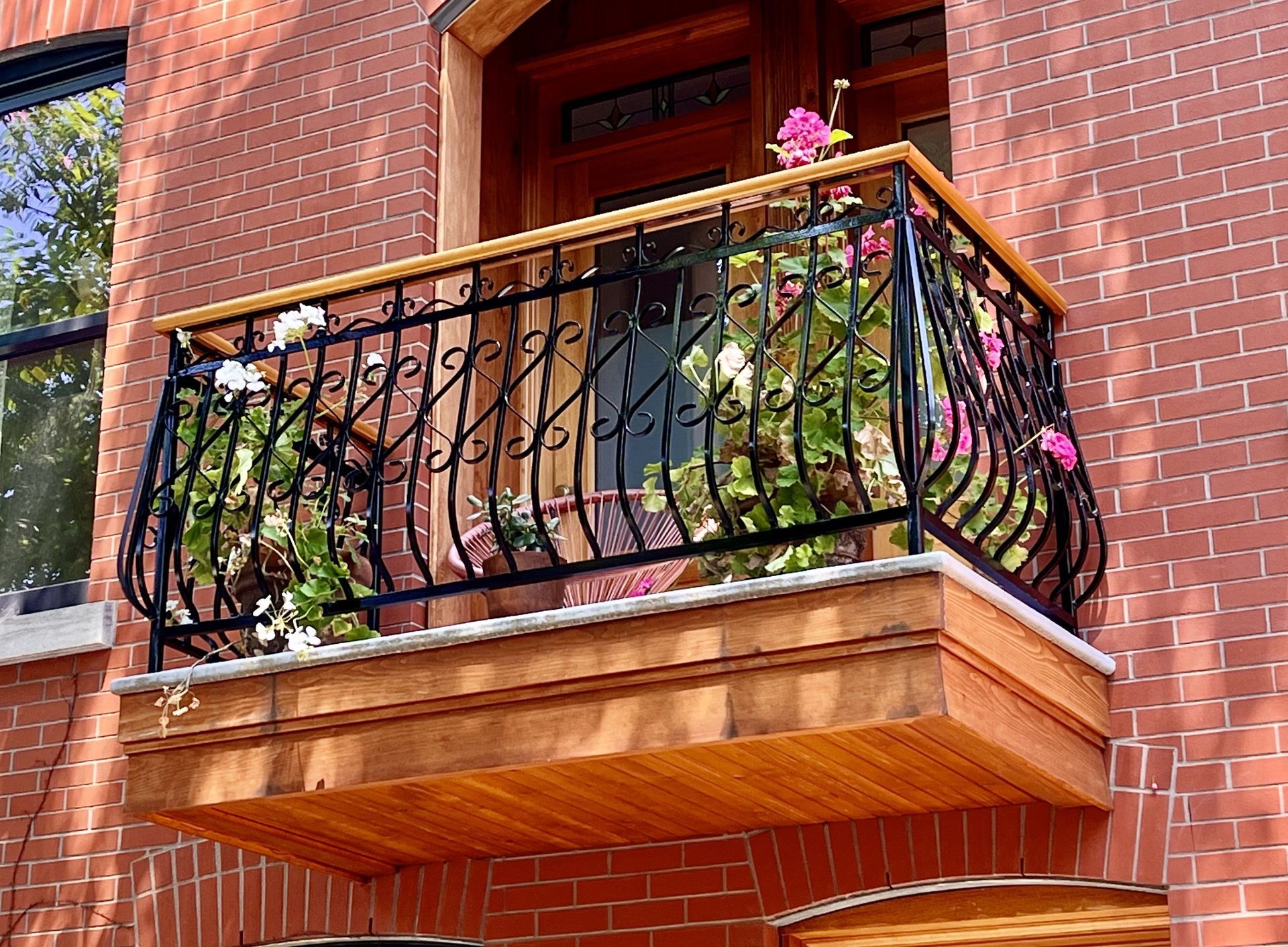 Brick building with a small balcony featuring ornate black railing, wood trim, and colorful flowers.