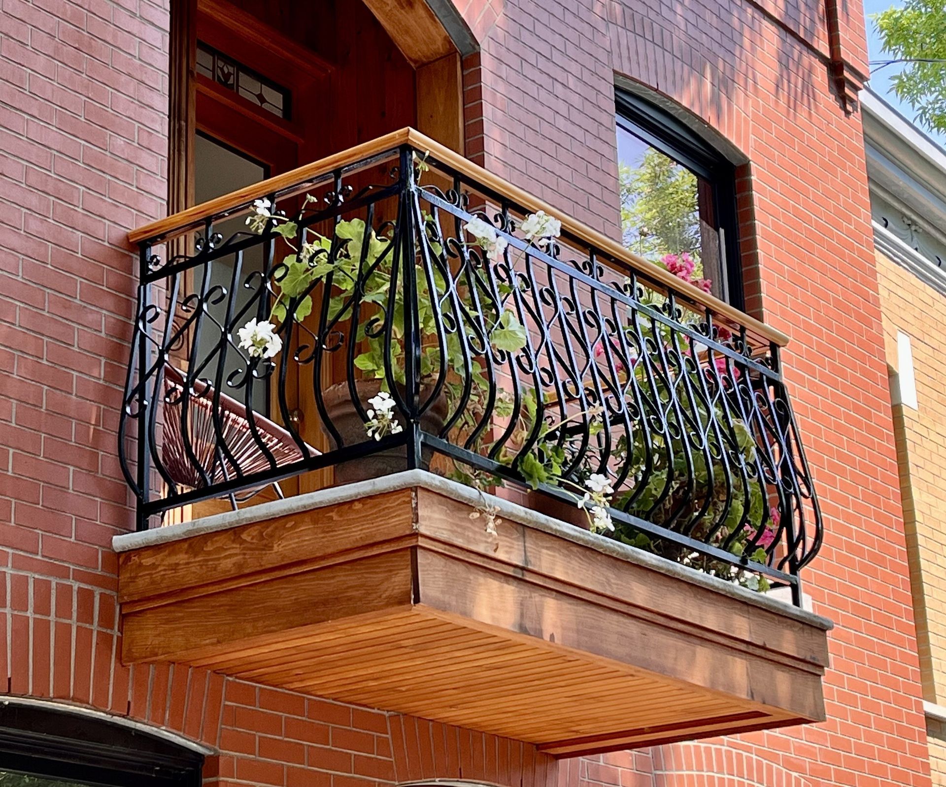 A small brick building with a wooden balcony decorated with black wrought iron and white flowers.