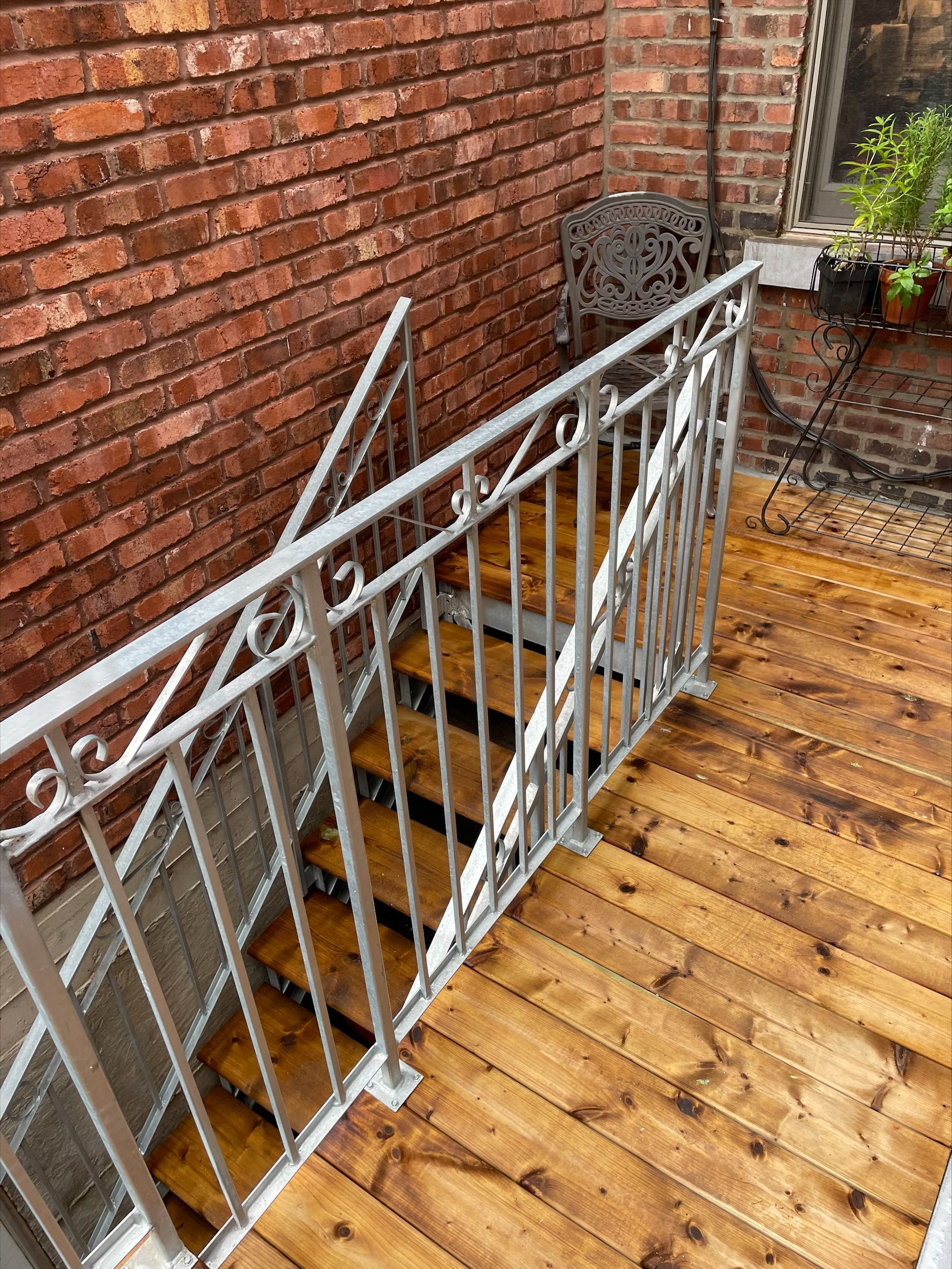 Wooden staircase with metal railing next to a brick wall.