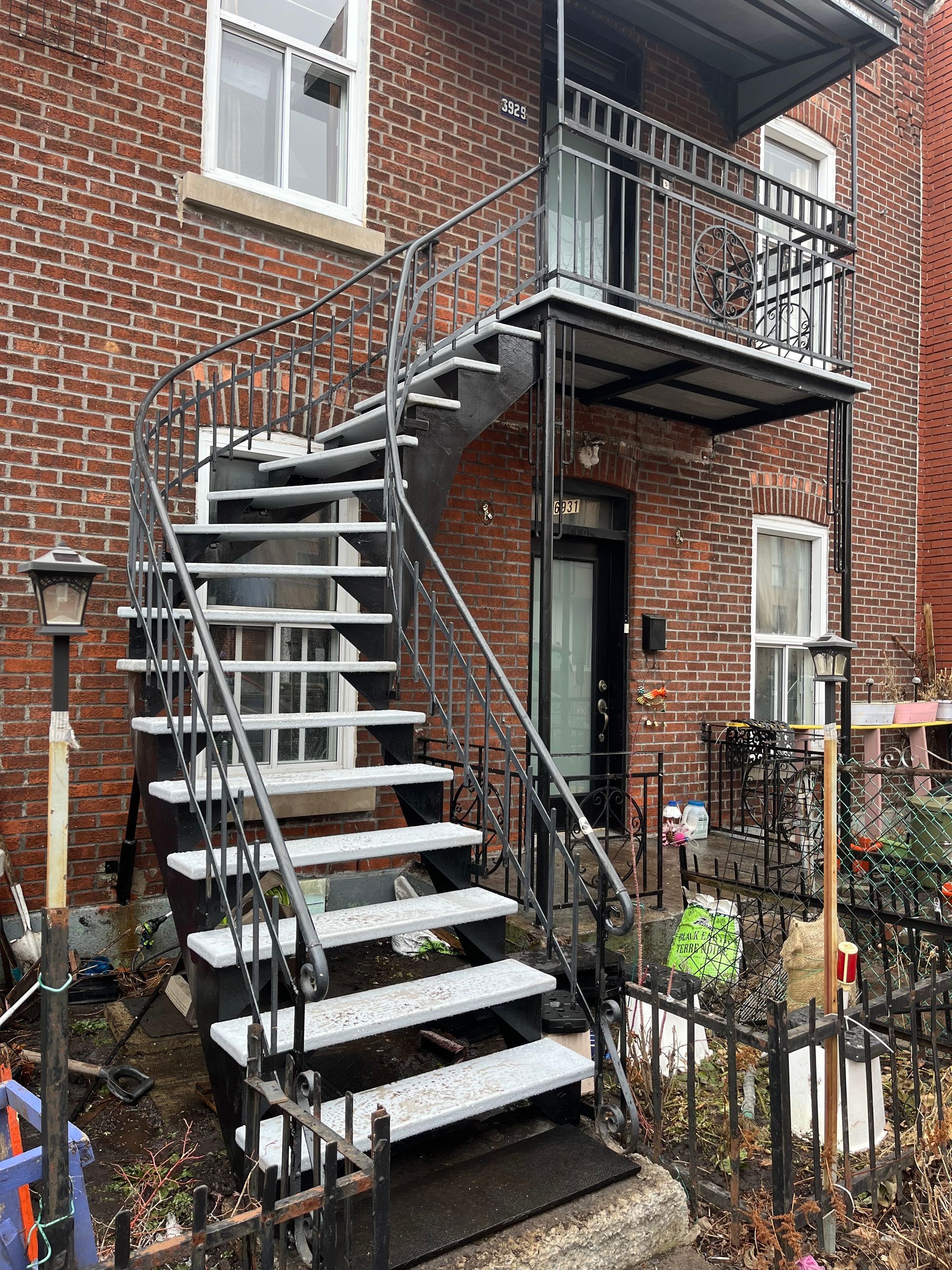 Vue extérieure d'un bâtiment en briques avec un escalier de secours en métal noir menant à un balcon et à une porte d'entrée.