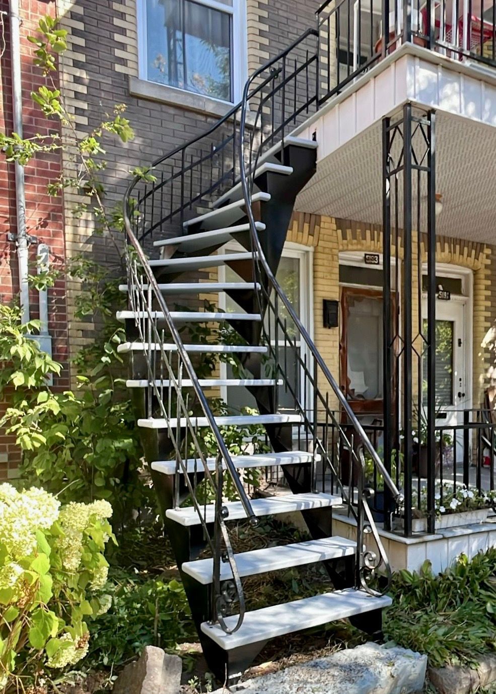 Escalier extérieur en métal menant au porche d'un bâtiment, adossé à une façade en briques et en bardage.