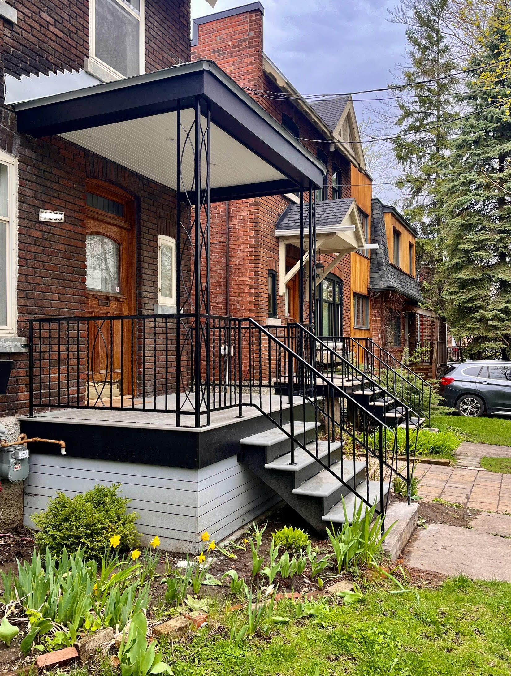 Brick house with porch and steps; black railings, gray steps, and a black awning.