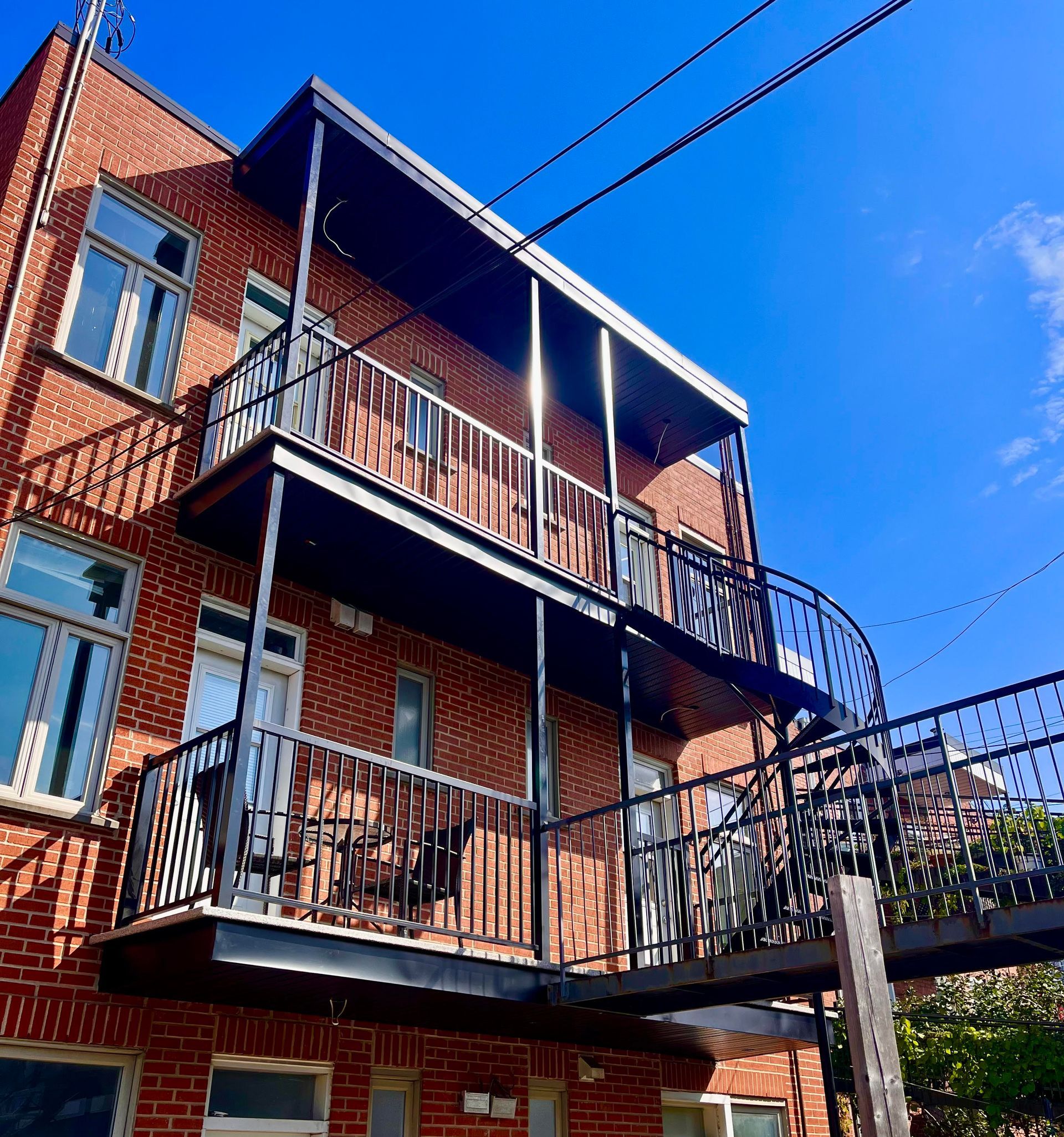Bâtiment en briques avec balcons en métal noir et un escalier en colimaçon contre un ciel bleu vif.