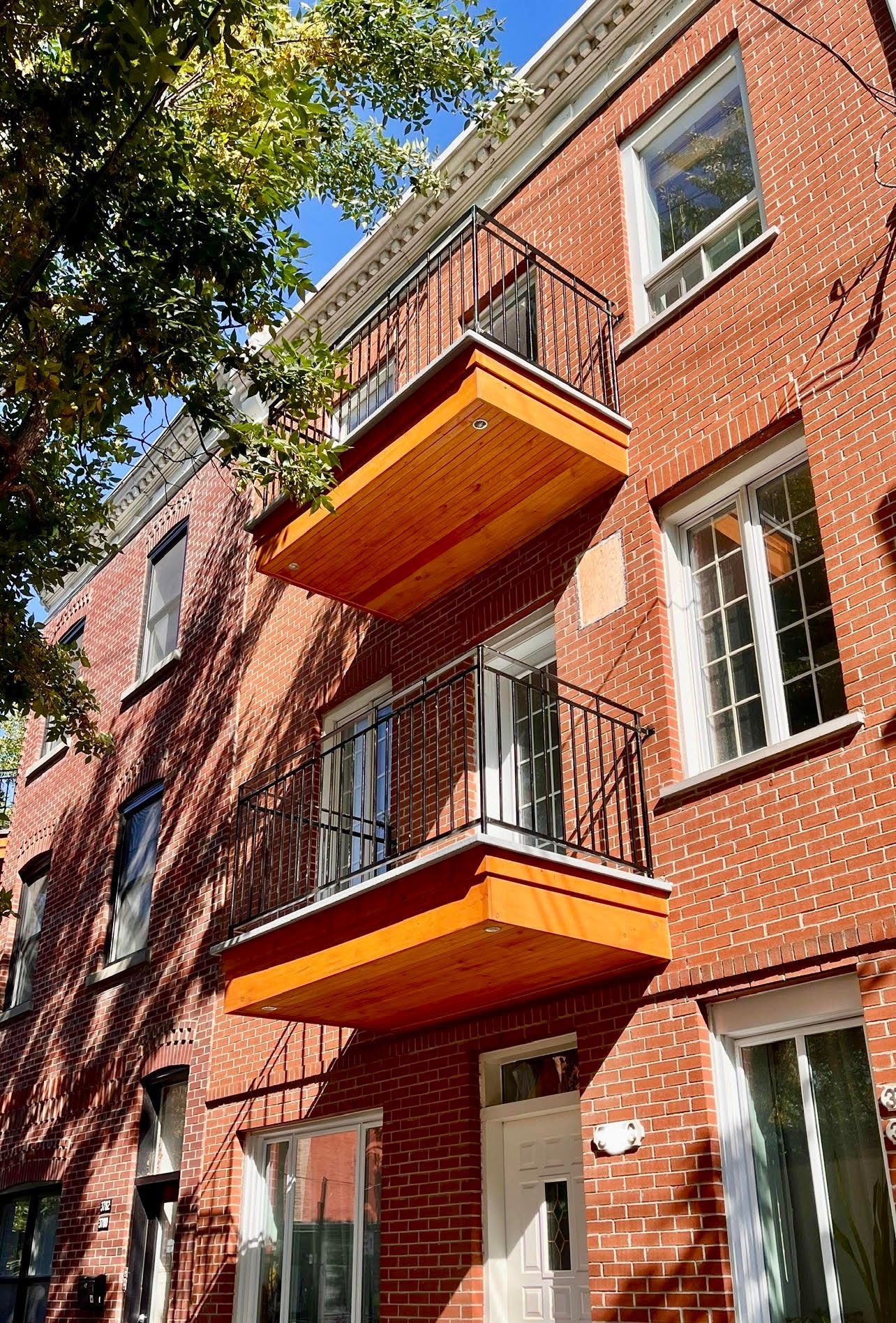 Deux escaliers extérieurs sur des bâtiments en brique et en pierre, l'un en métal, l'autre en bois, avec un petit carré de pelouse.