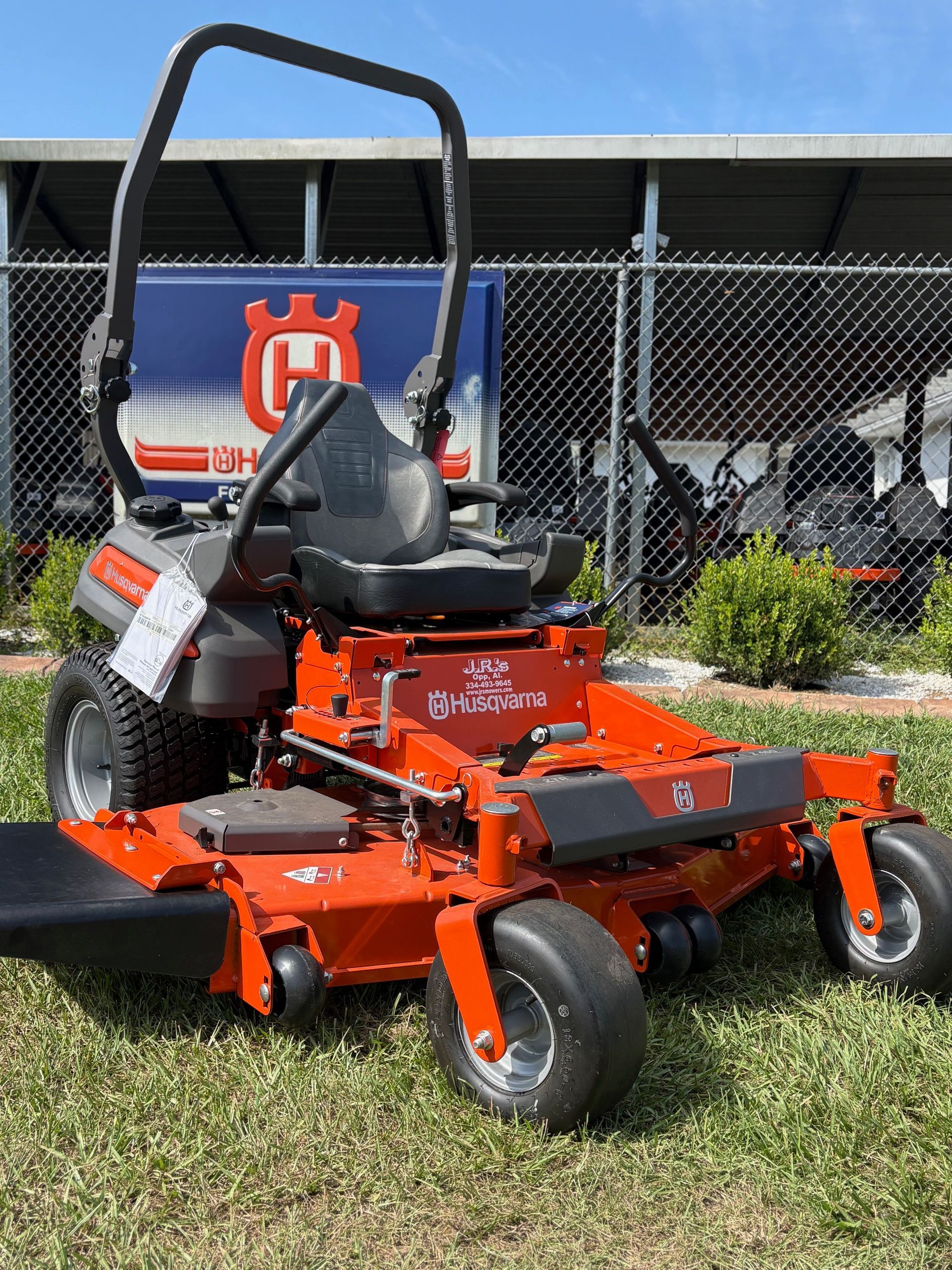 Orange Husqvarna zero-turn riding lawnmower on grass, with Husqvarna sign in background.