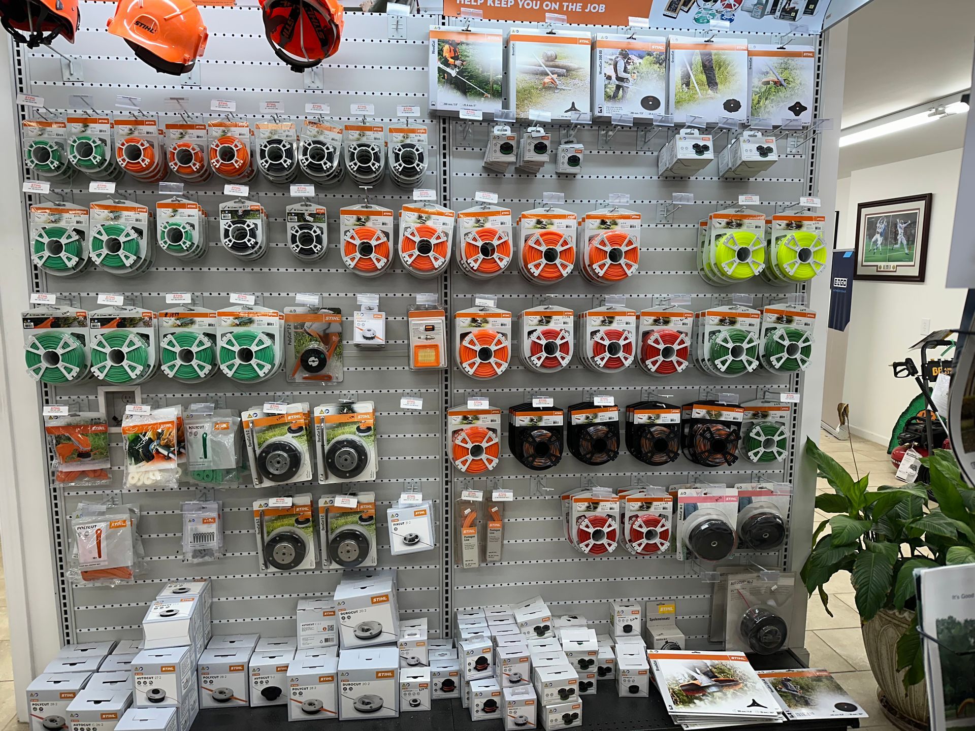 Shelving unit displaying various trimmer heads and accessories in a retail setting; orange, green, and black packaging.