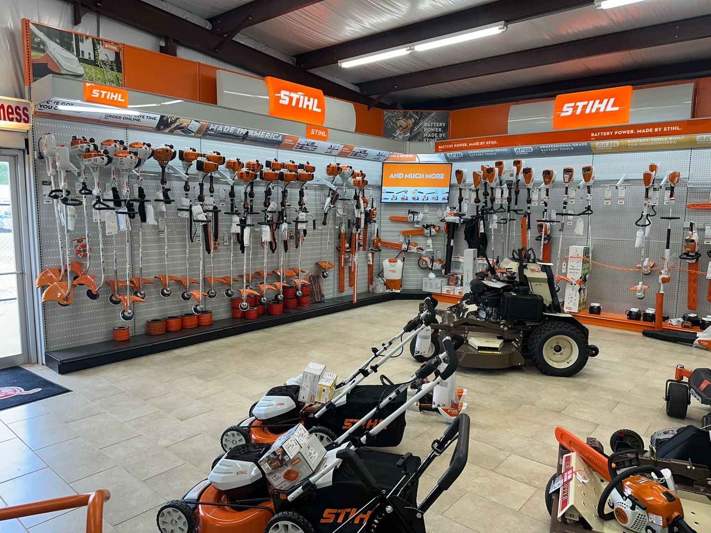 Inside a hardware store, Stihl lawn equipment is displayed on shelves and floor.
