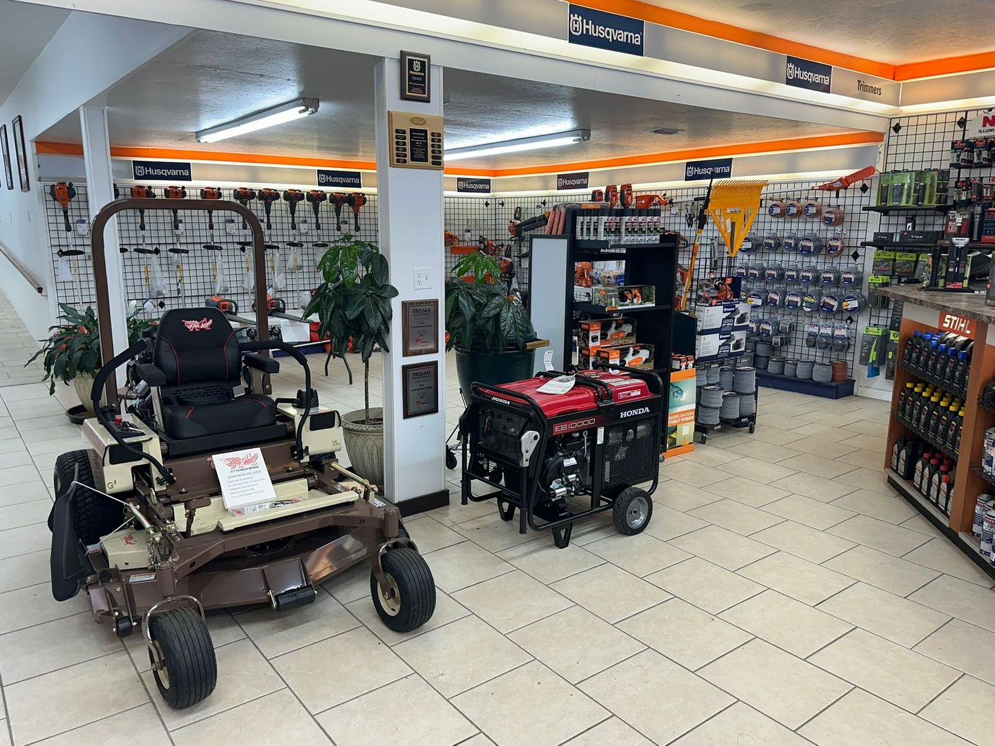 Inside a hardware store: zero-turn mower, generator, tools on shelves, and various gardening supplies.