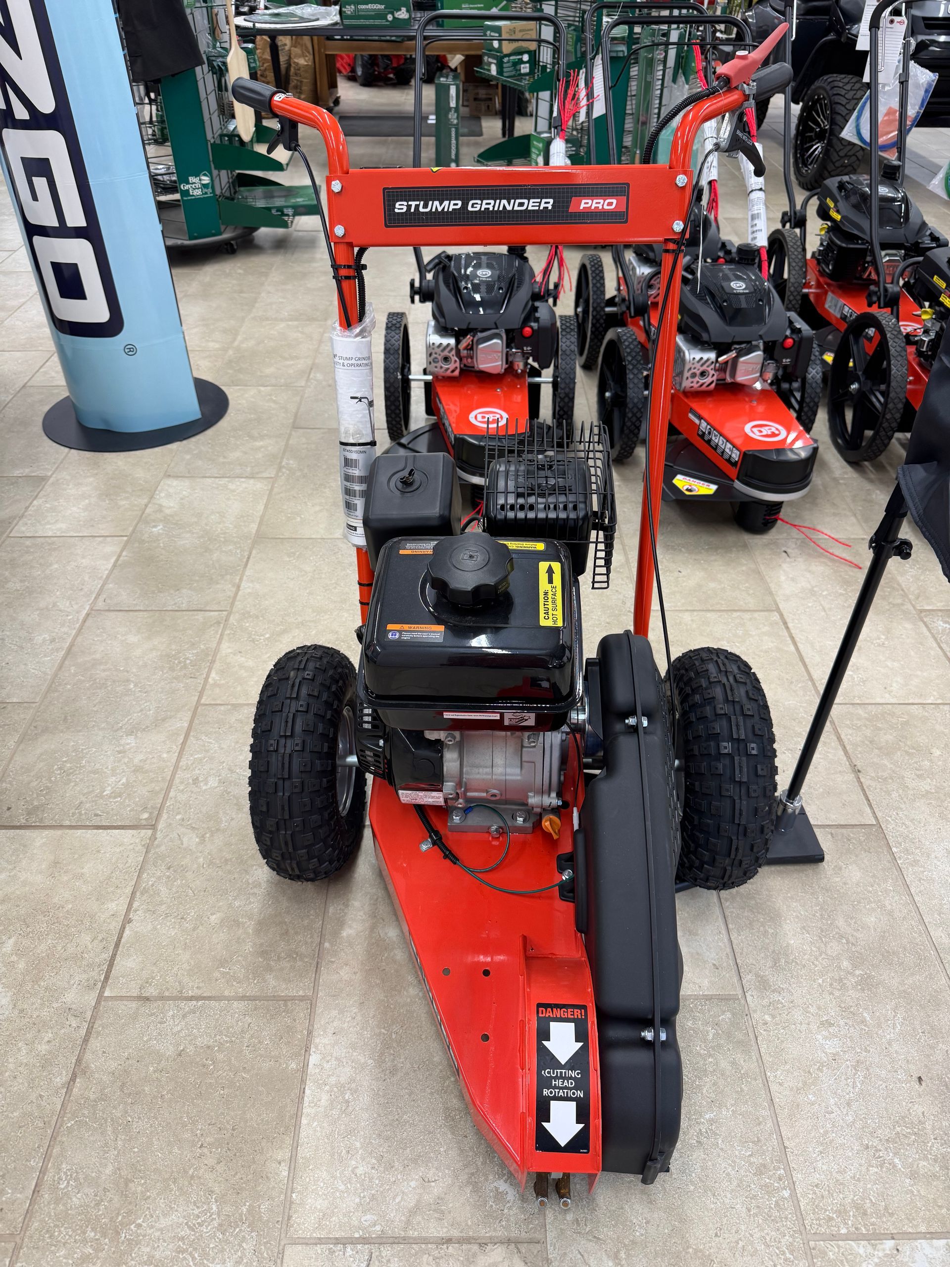 Orange stump grinder with black tires and engine. Inside a store on tile floor.
