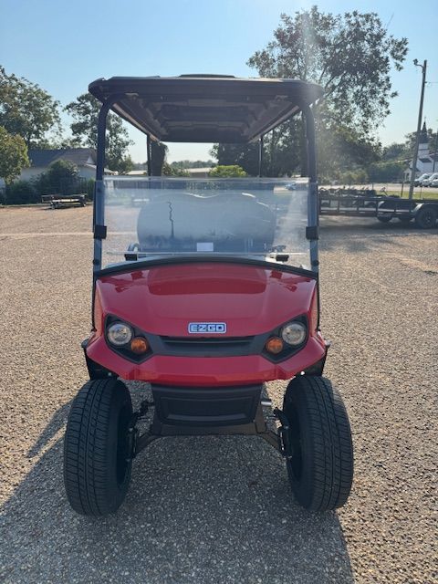 Red six-seater golf cart on gravel, with black roof, seats, and wheels.  Other golf carts in the background.