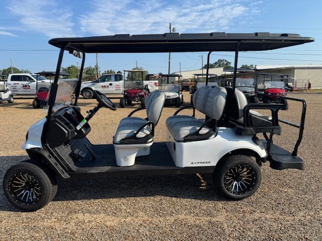 White 6-passenger golf cart with black roof, black and gray seats, and black rims parked outside.