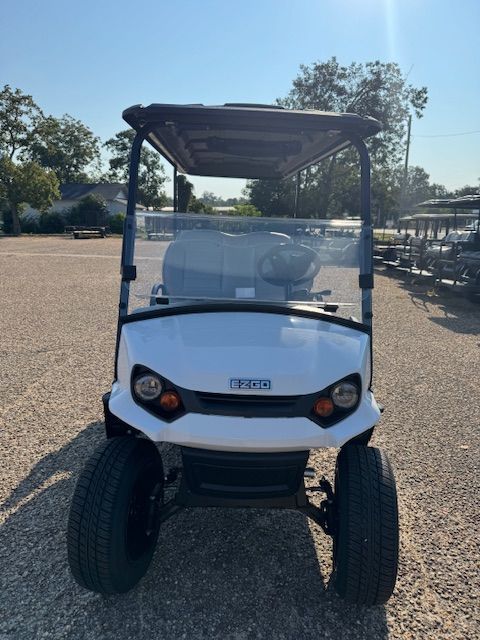 White 6-passenger golf cart with black roof, black and gray seats, and black rims parked outside.