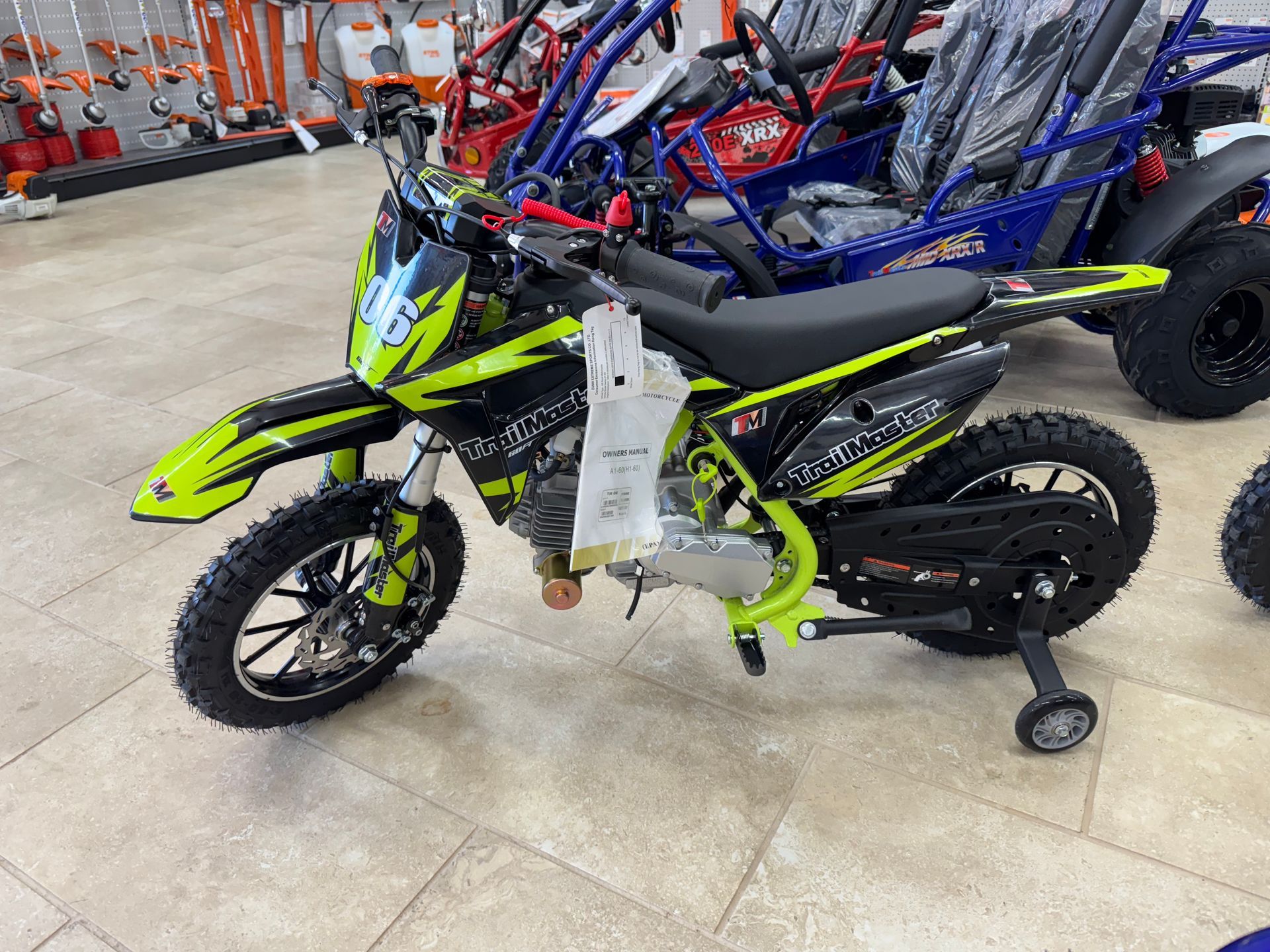 A small green and black dirt bike with training wheels in a store.