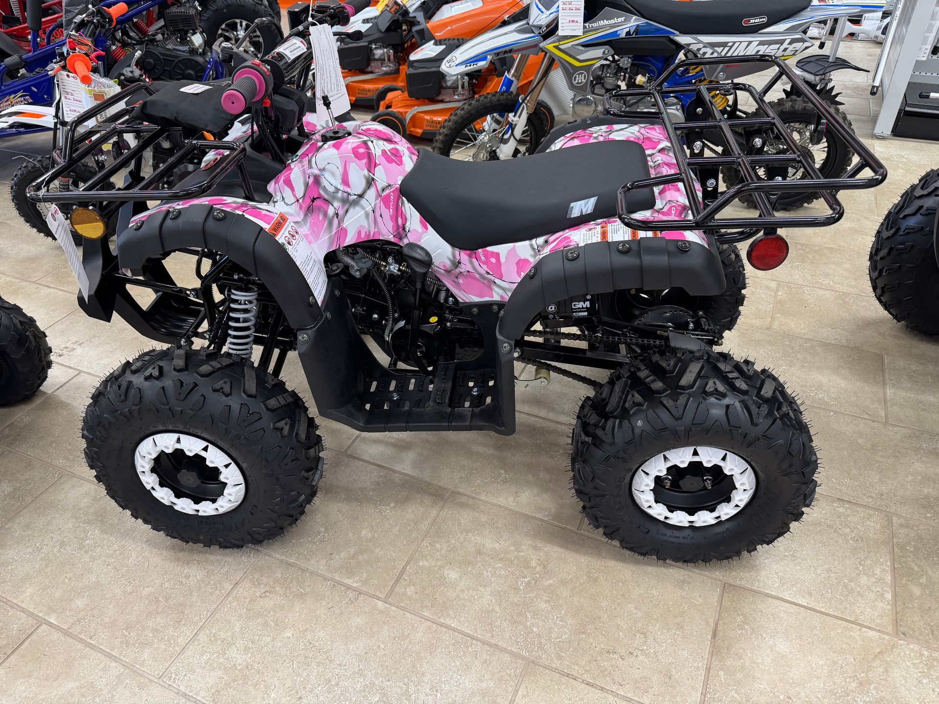Pink camouflage ATV with black rack and white-rimmed tires on display.