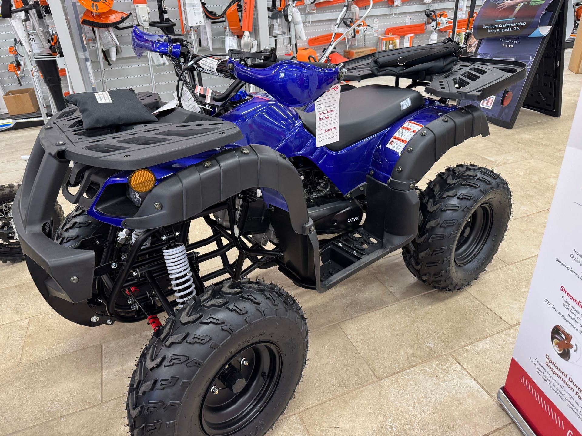 Blue ATV with black tires and front and rear storage racks in a store.