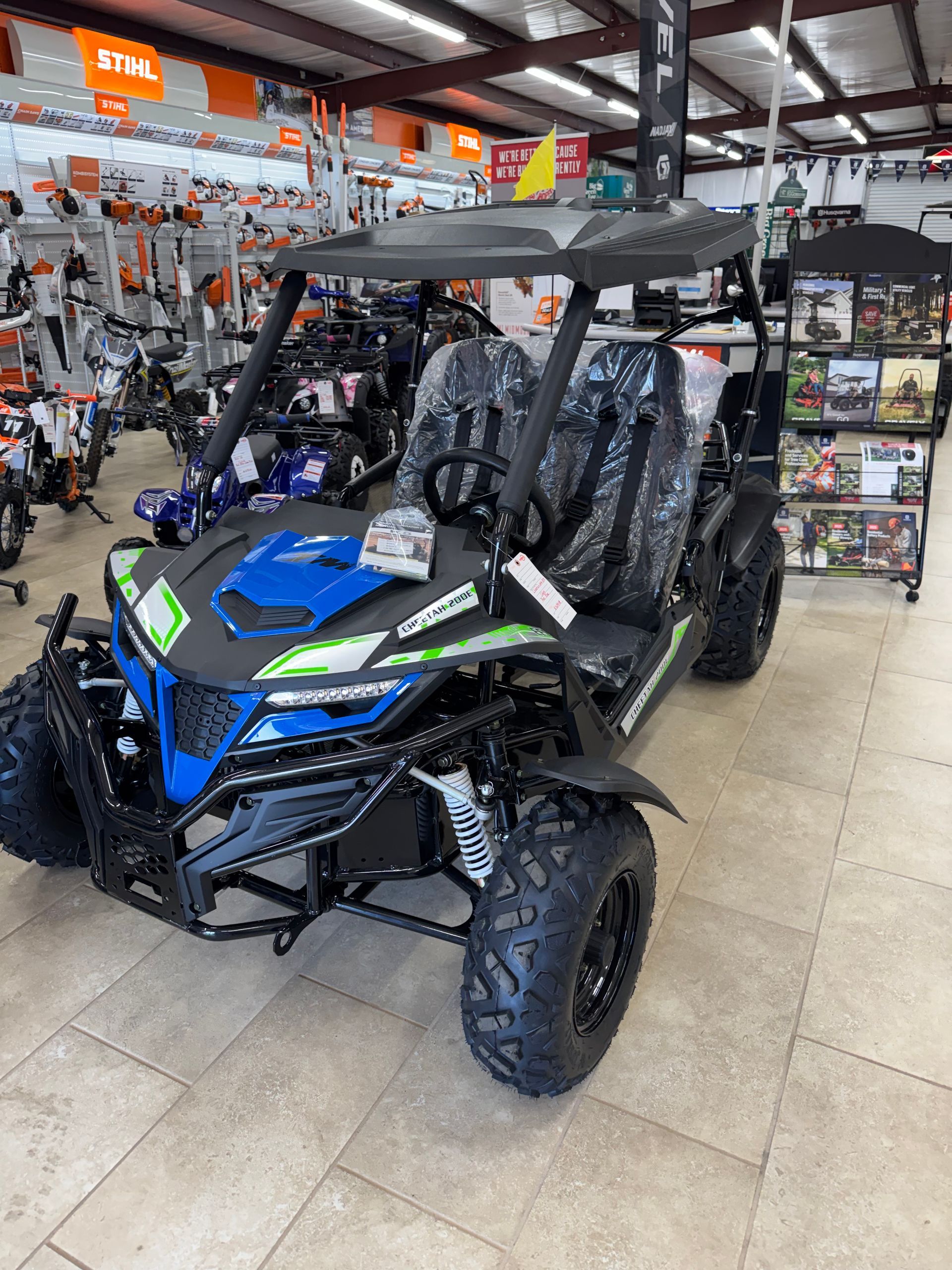 Blue and black go-kart on display at a store, with green accents and black tires.