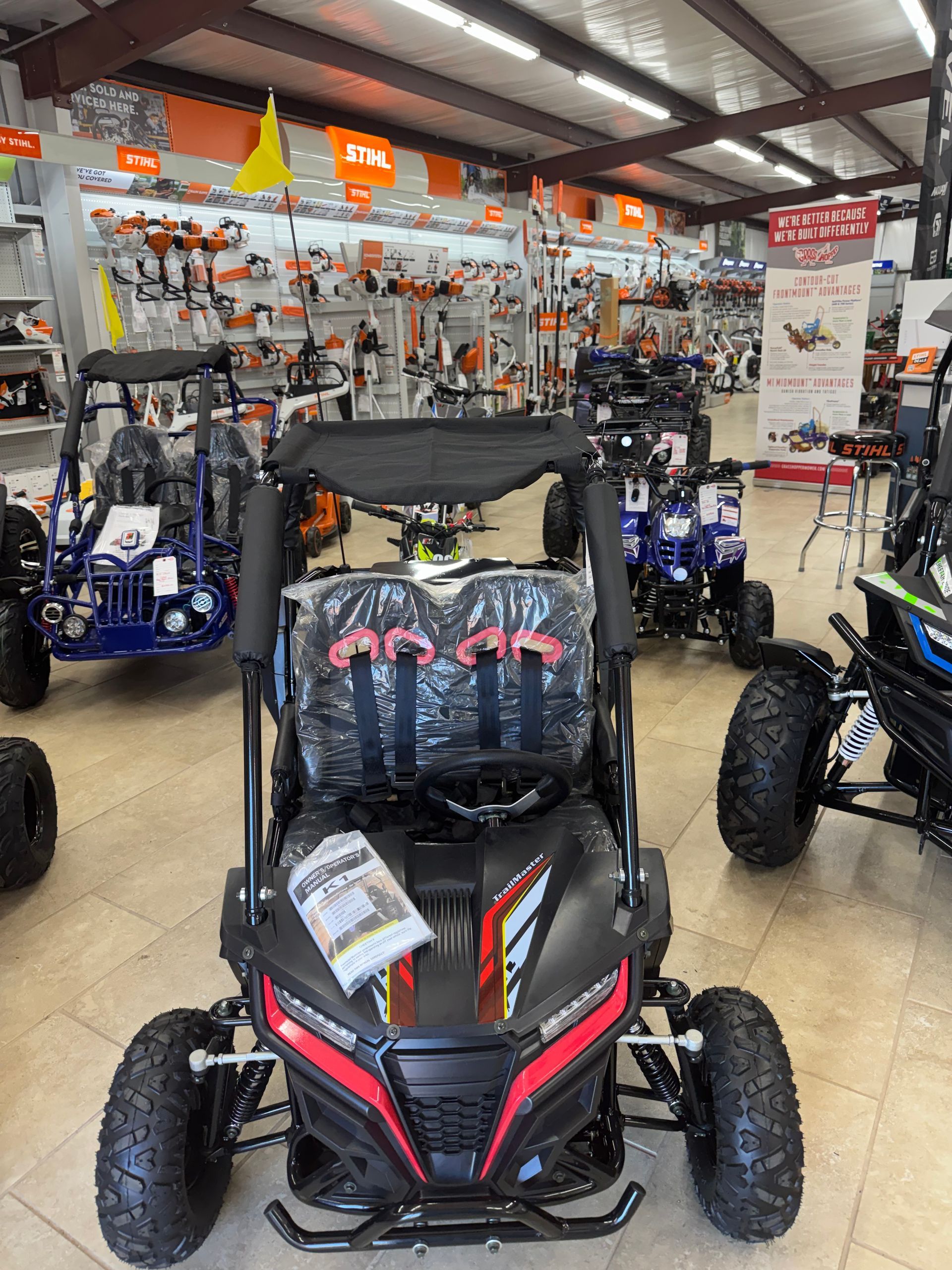Black and red go-kart in a store, surrounded by other vehicles and tools.