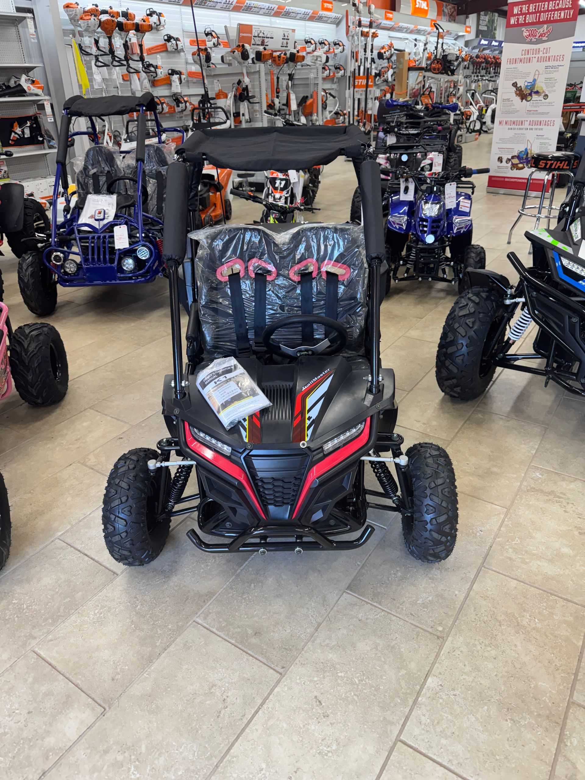 Black and red go-kart in a store, surrounded by other vehicles and tools.