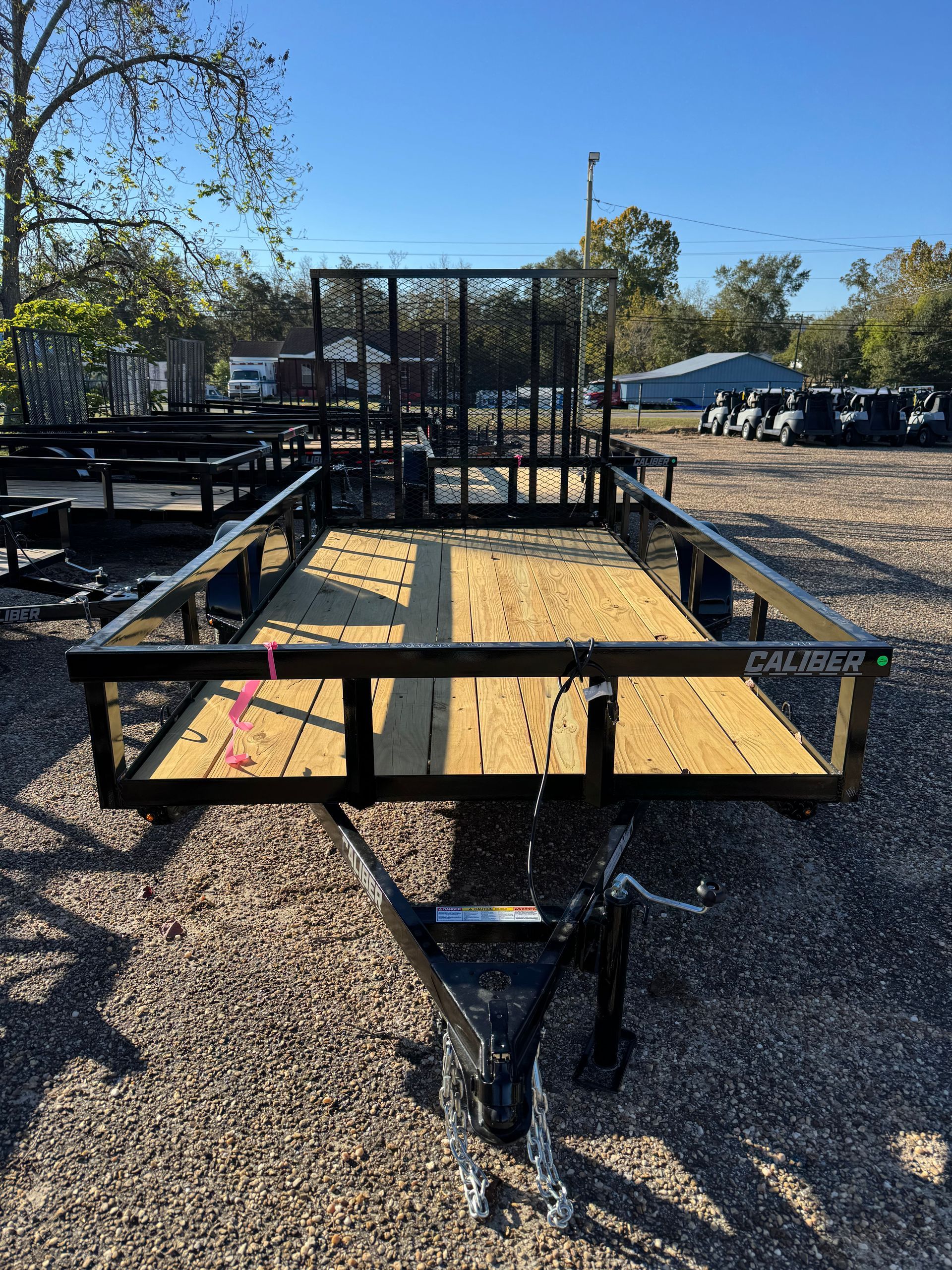Black utility trailer with wooden deck, parked outdoors.