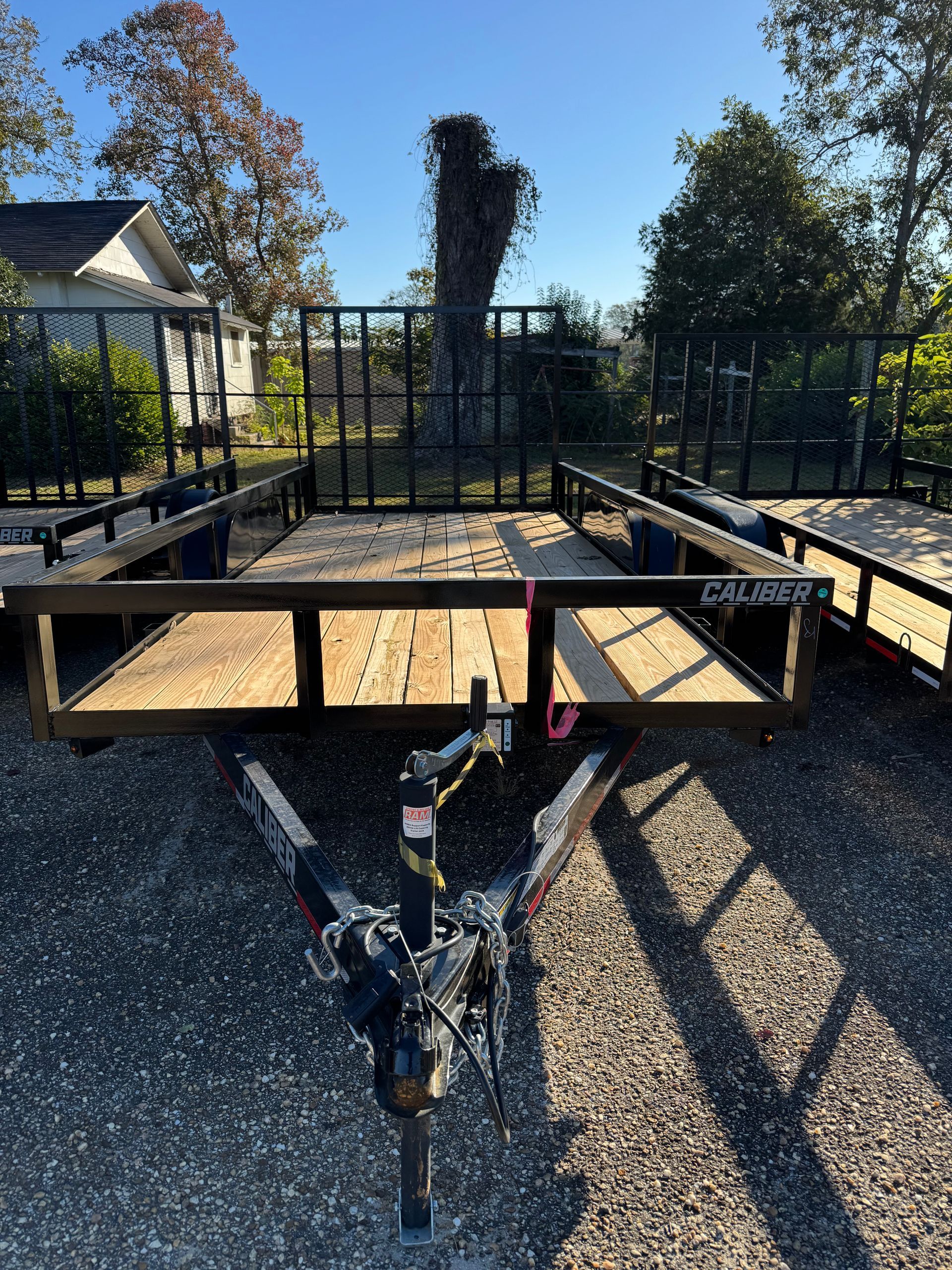 Black utility trailer with wooden deck, metal frame, and hitch, outdoors on a sunny day.