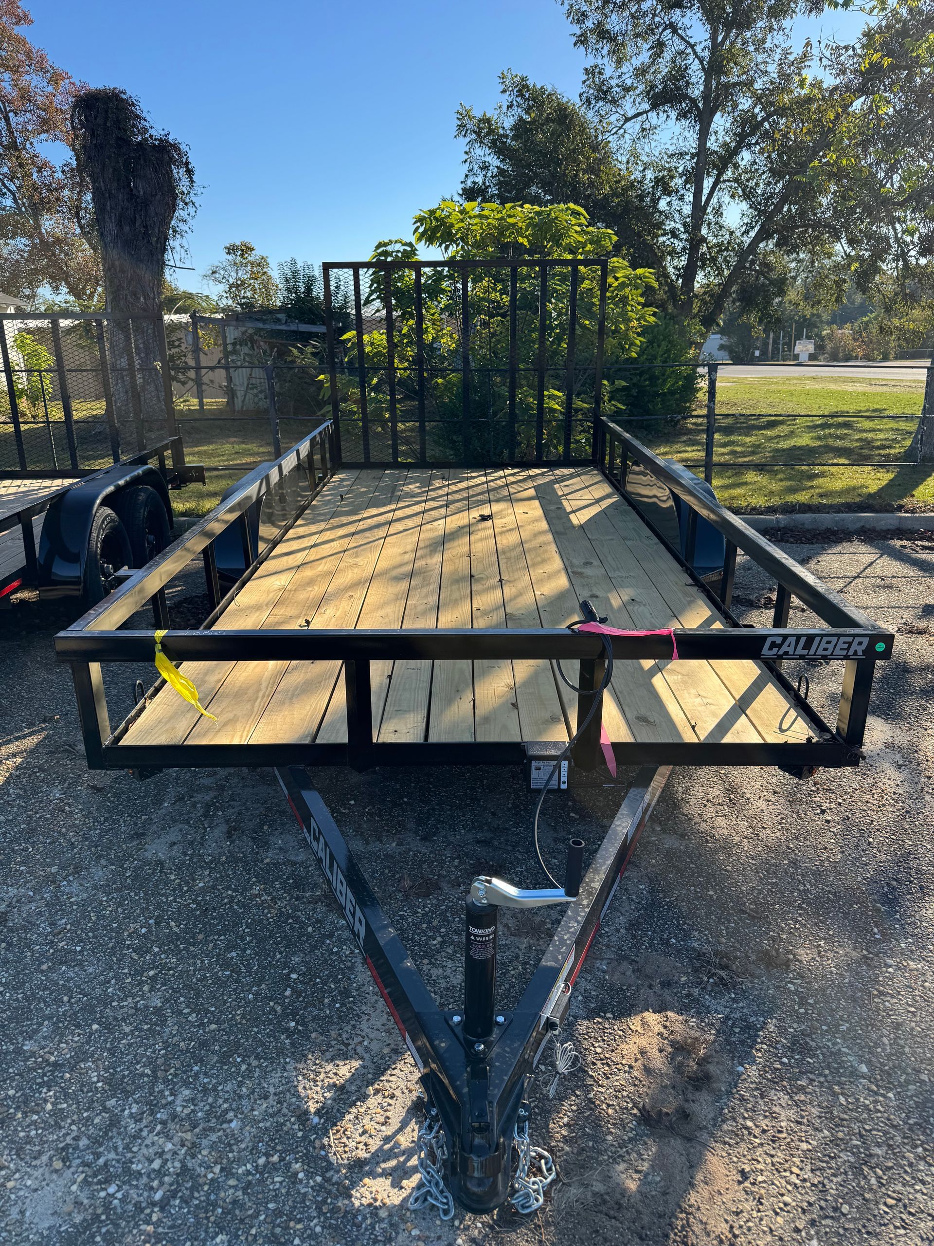 Black utility trailer with wooden deck, metal side rails, and a front cage. Outdoors.
