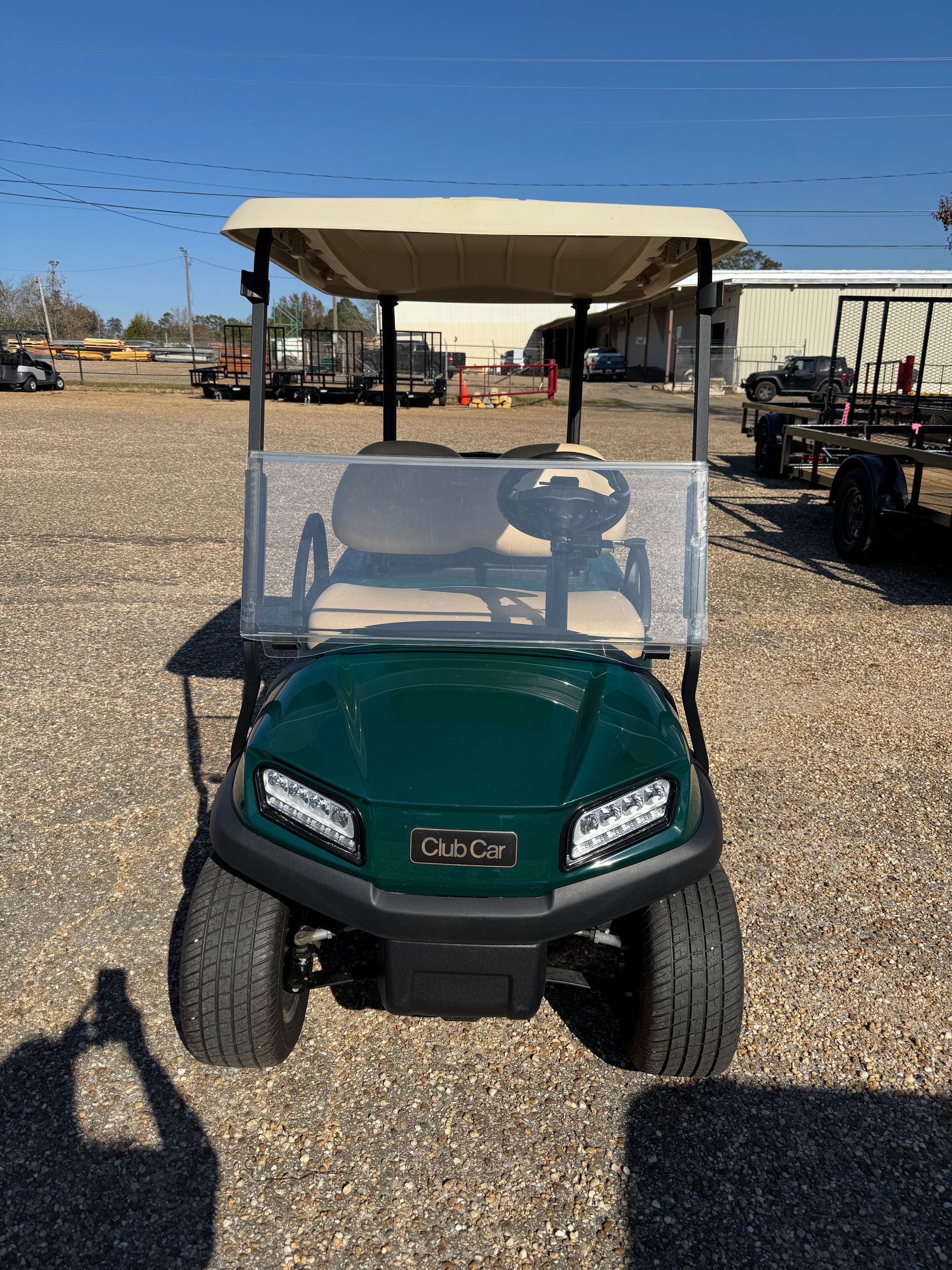 Green Club Car golf cart with tan roof, parked outside on a sunny day.