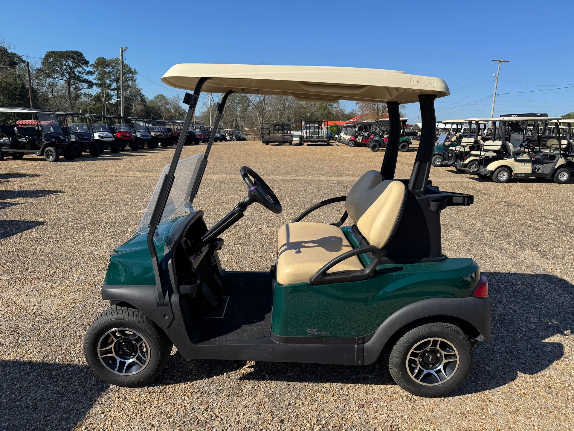 Green Club Car golf cart with tan roof, parked outside on a sunny day.